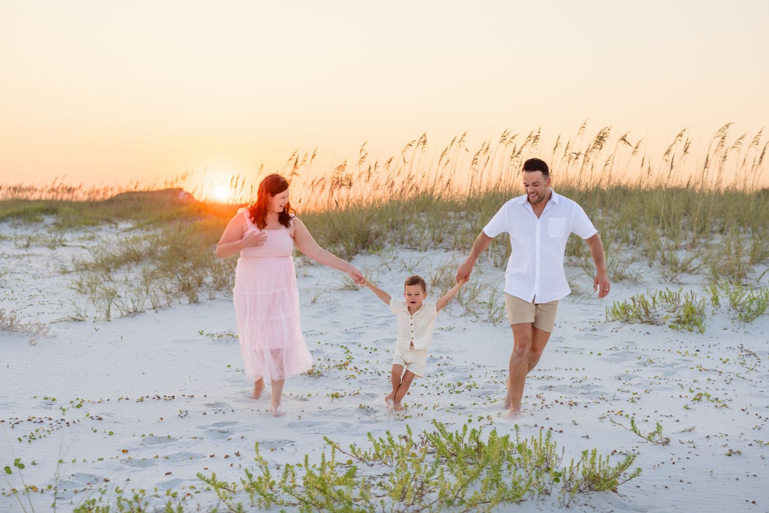 A family jumps together on a white sandy beach at sunset with ocean waves in the background.