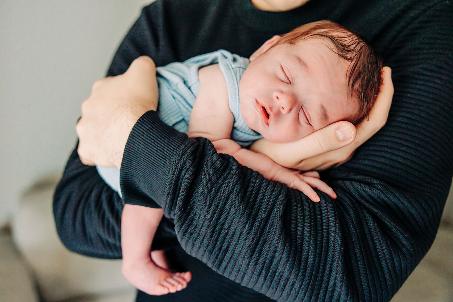 A baby sleeping peacefully in a blue onesie while resting on someone's arms.