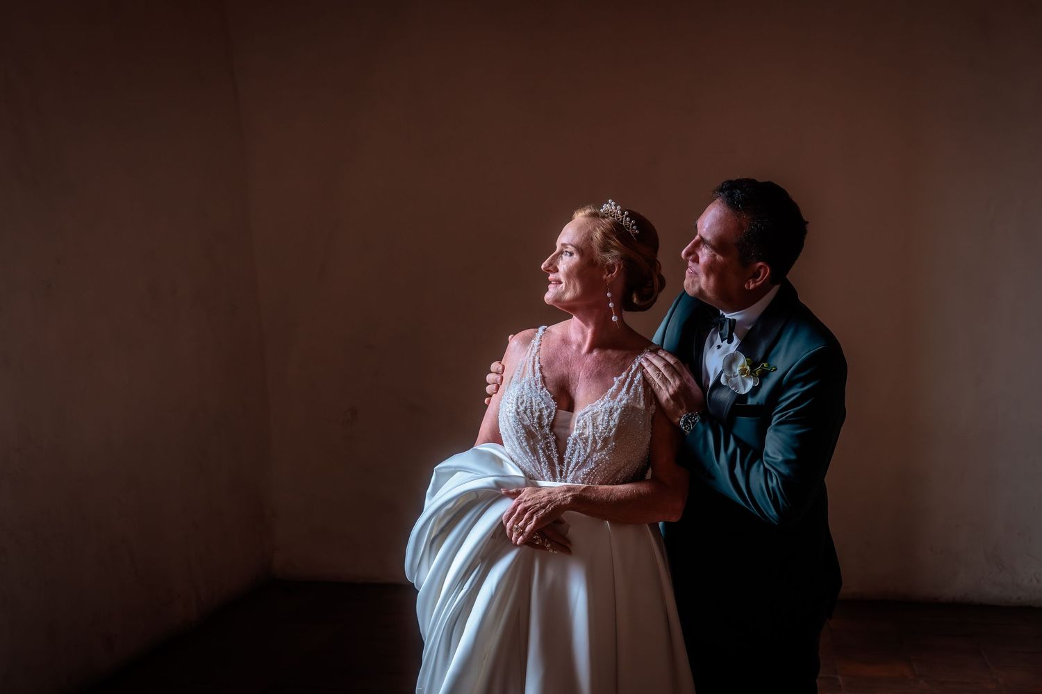 Intimate couple's portrait in warm lighting against a dark moody background.