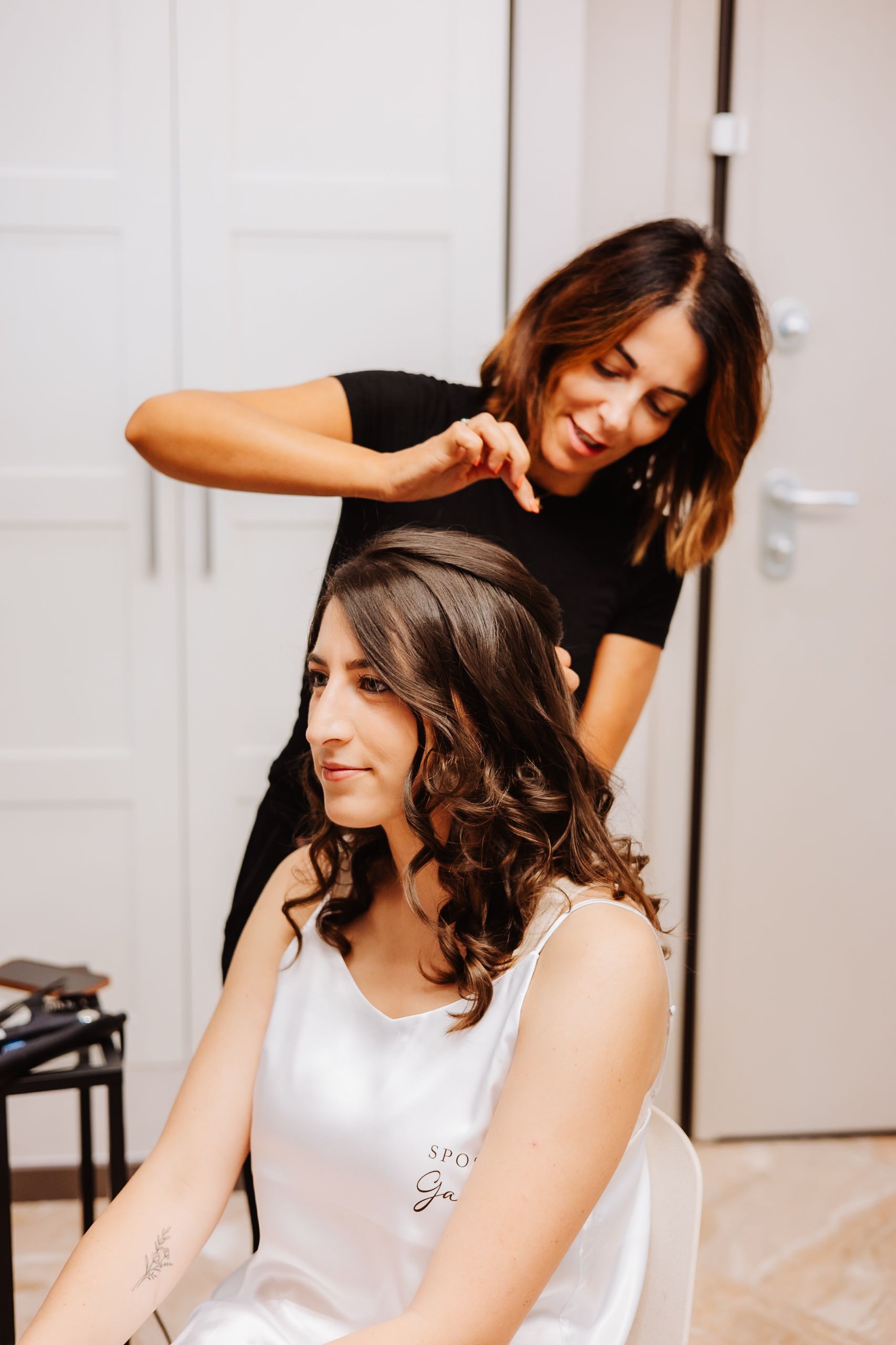 Hair styling session in progress showing curled brunette hair being styled in a bright room.
