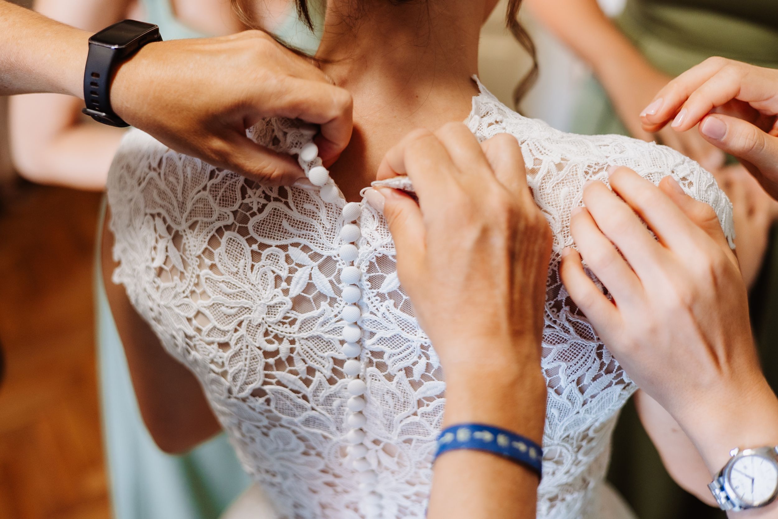 Close-up view of hands fastening delicate white lace buttons on a wedding dress bodice.