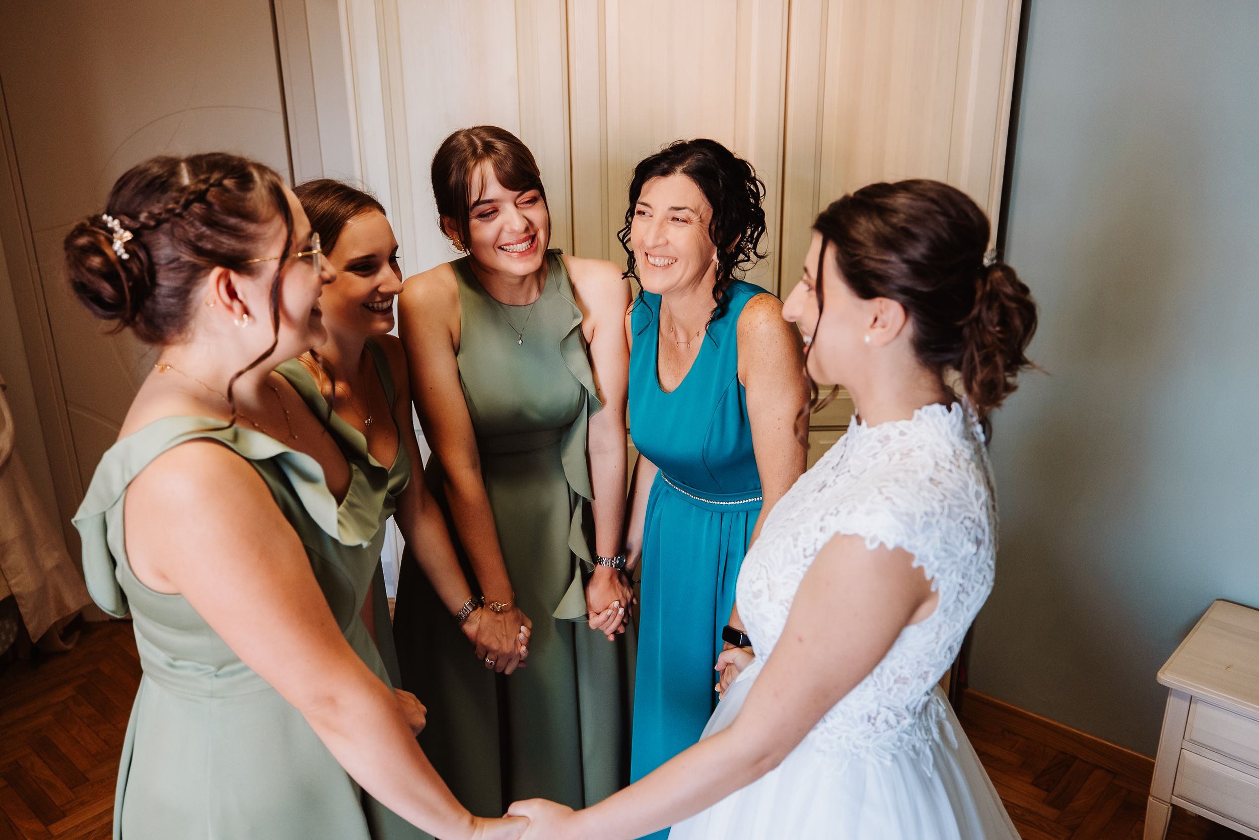 Bridesmaids in turquoise dresses help the bride get ready in a sunlit room before the wedding ceremony.