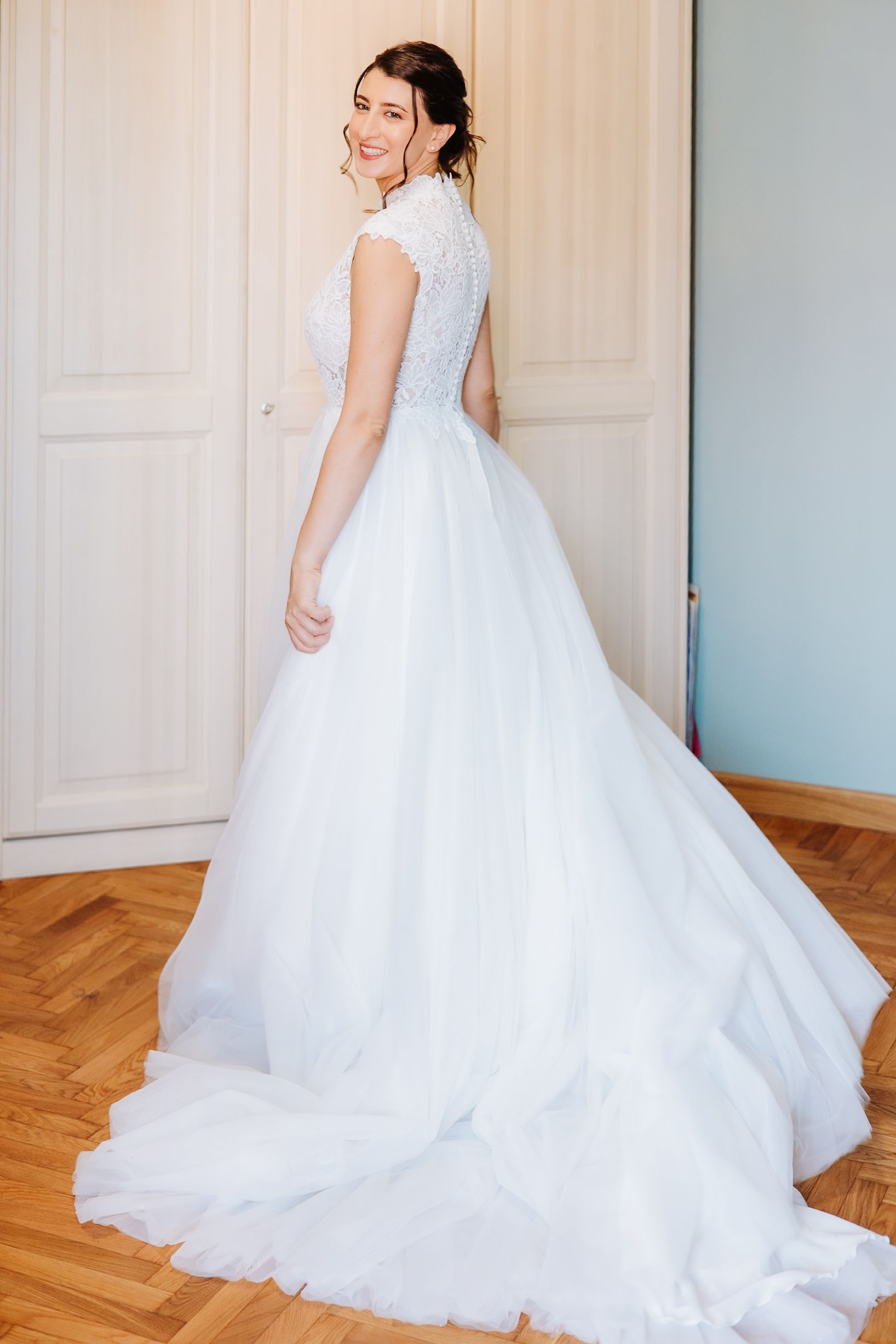 A stunning white wedding gown with lace bodice and flowing tulle skirt shown from the back on a hardwood floor.
