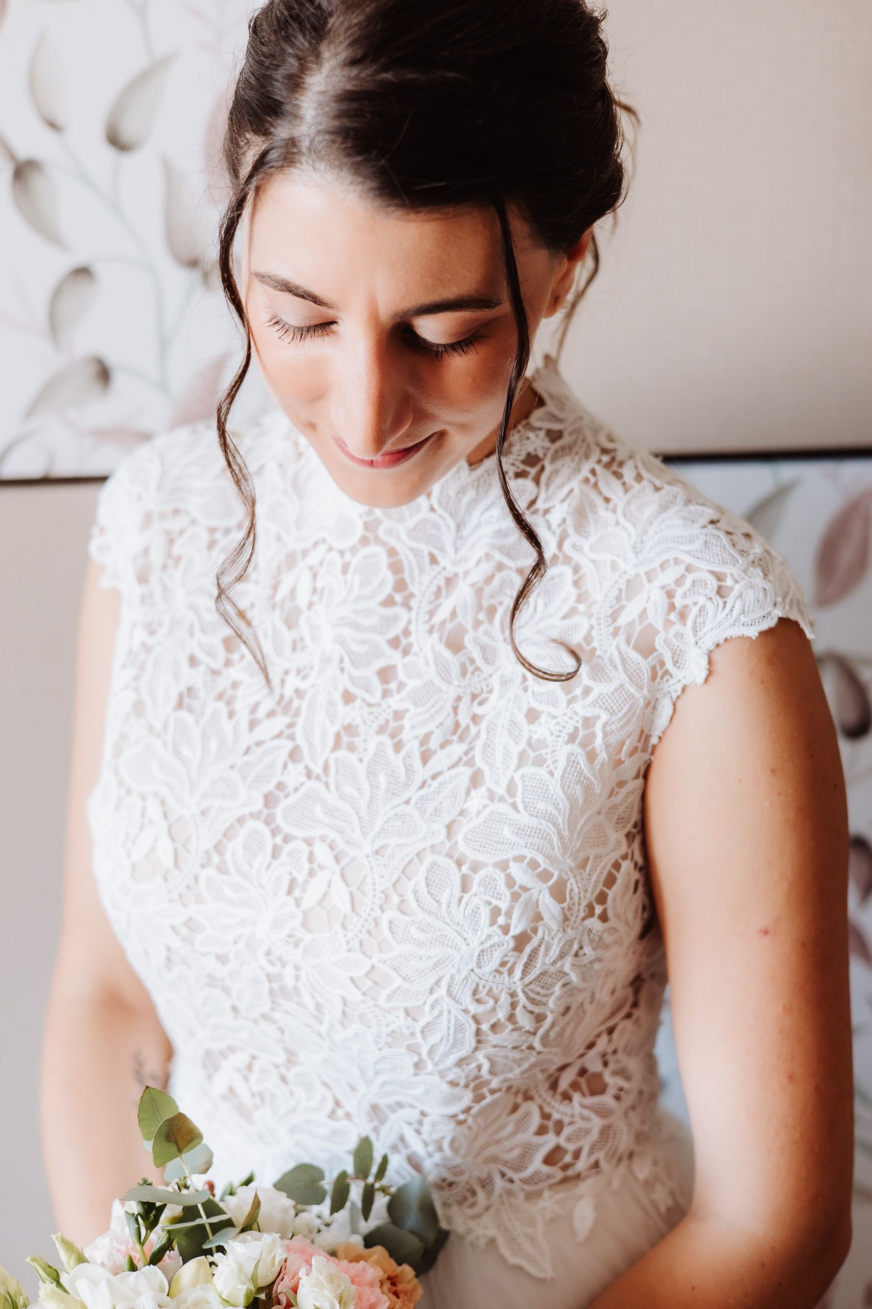 Close up view of a bride in a white lace wedding dress looking down at her bouquet.
