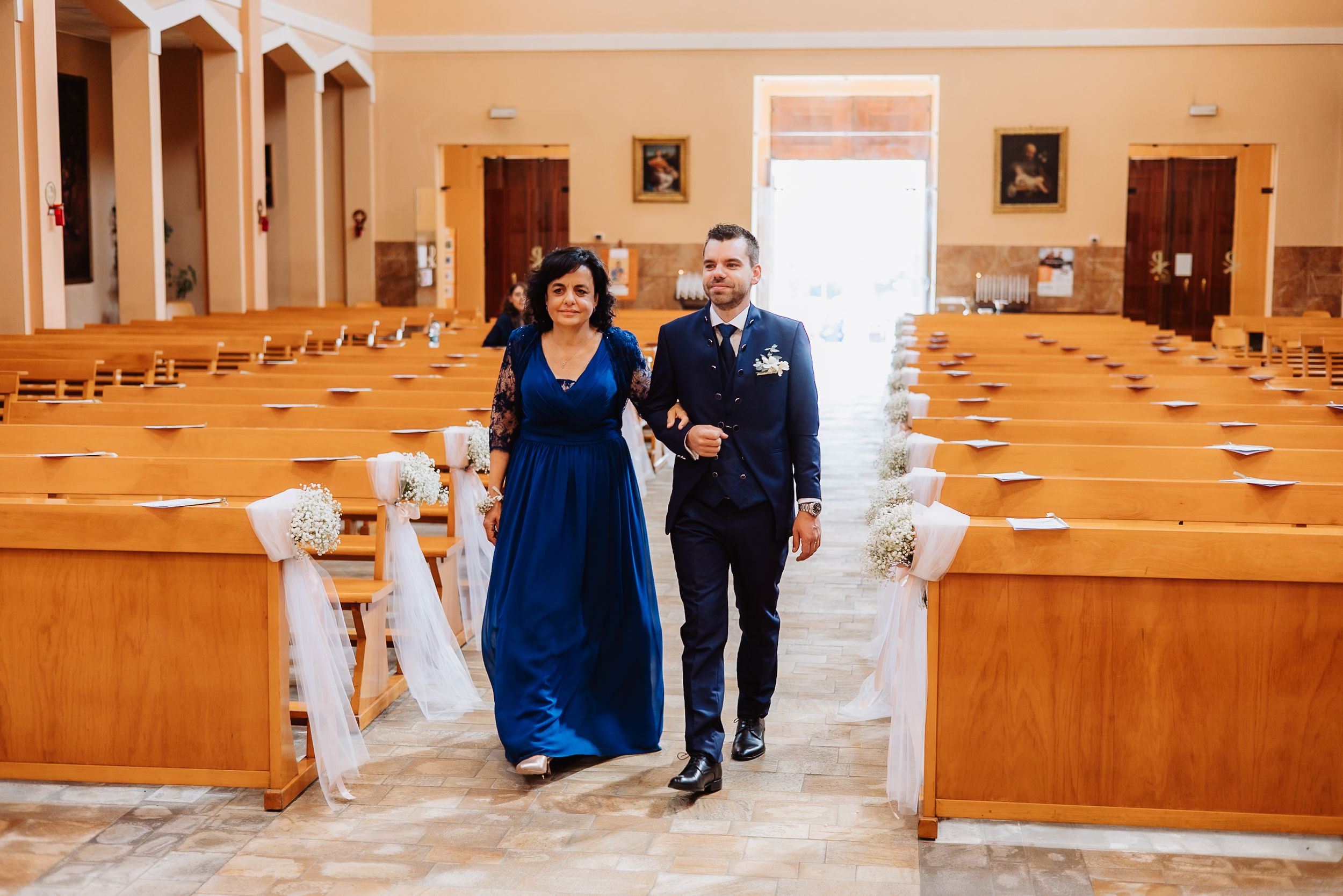 A bride and groom walk down a church aisle lined with wooden pews and natural lighting streaming through windows.