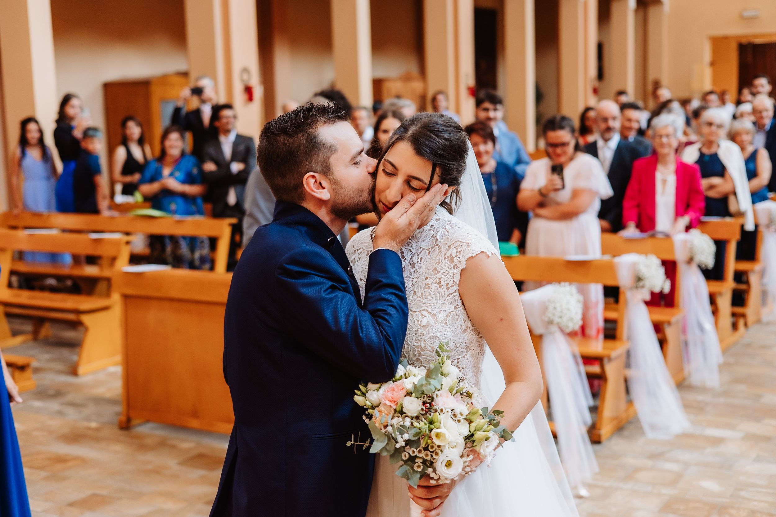 A couple shares their first kiss as newlyweds at the altar while wedding guests look on in a church ceremony.