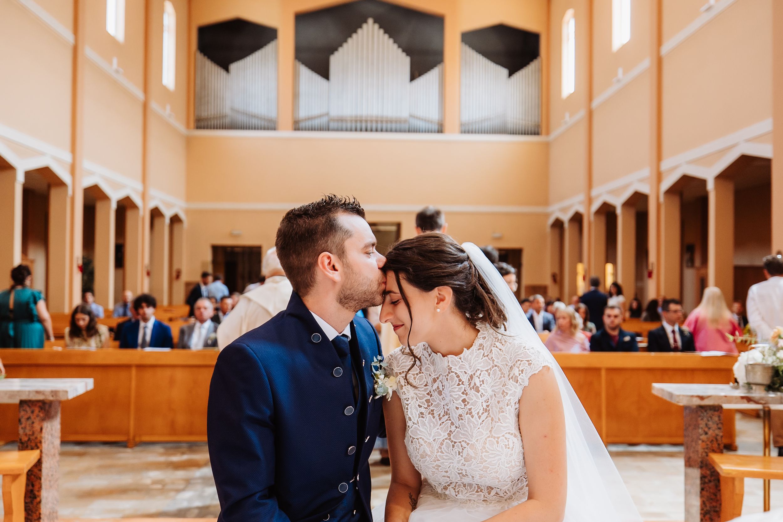 A bride and groom share a romantic kiss during their wedding ceremony in an elegant church sanctuary.