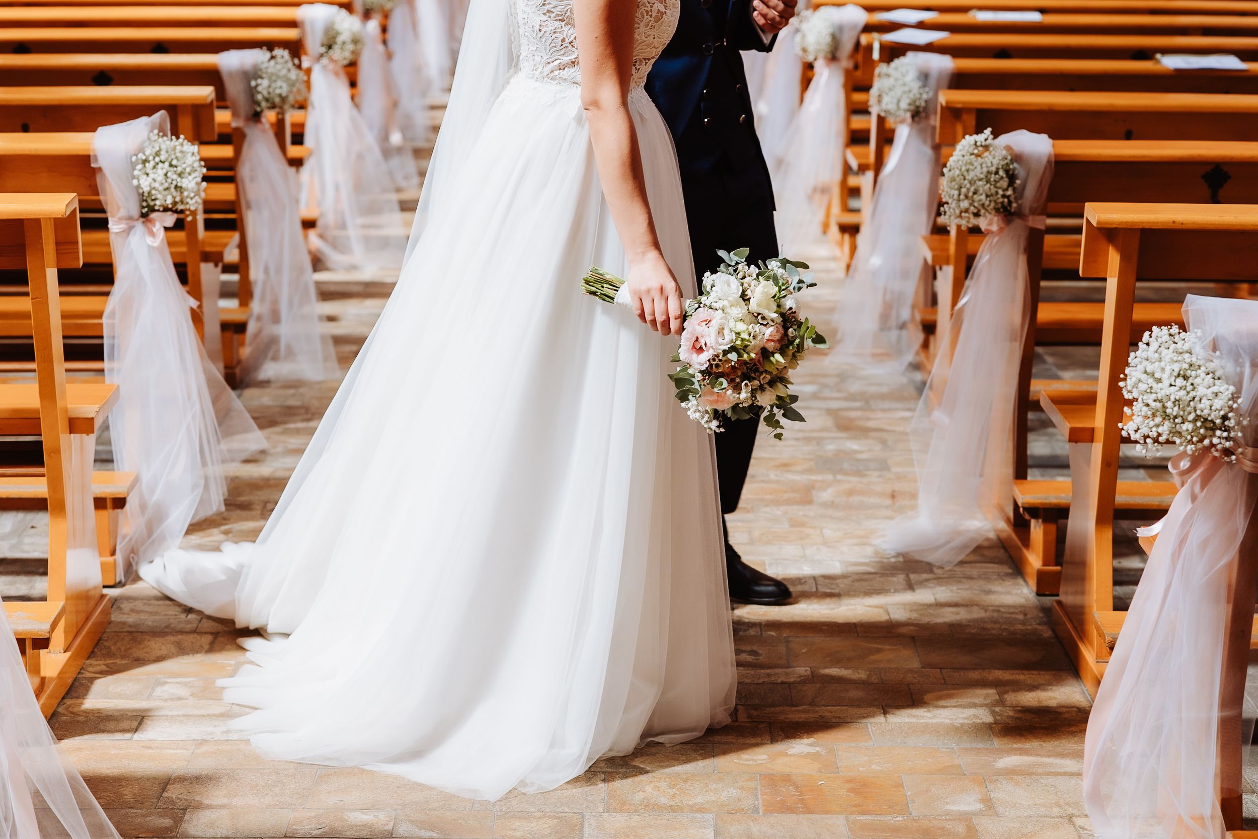 Wedding ceremony aisle decorated with white tulle and baby's breath flower bouquets in a wooden church interior.