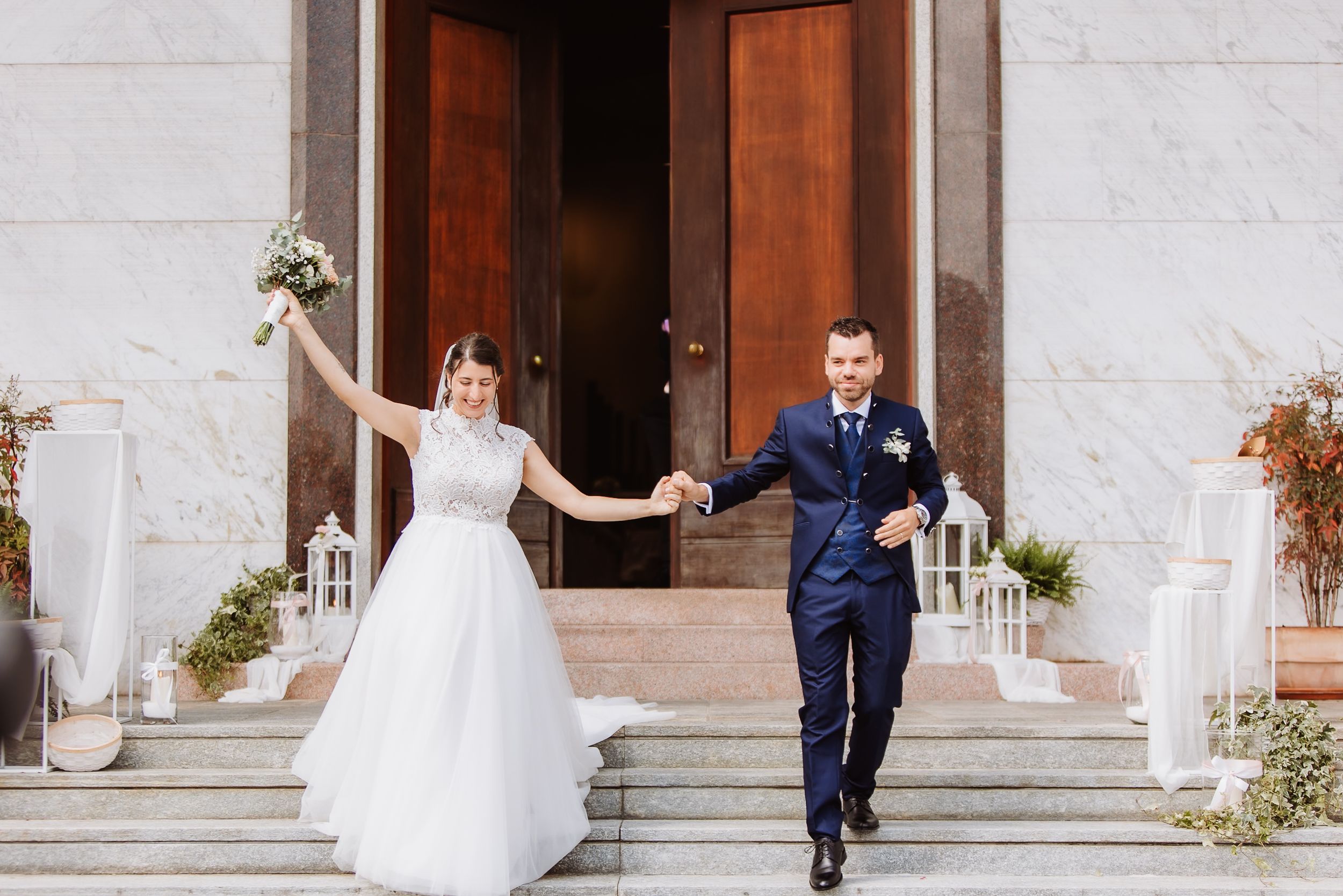 Bride and groom walking together outside a grand church entrance with stone columns and stairs.