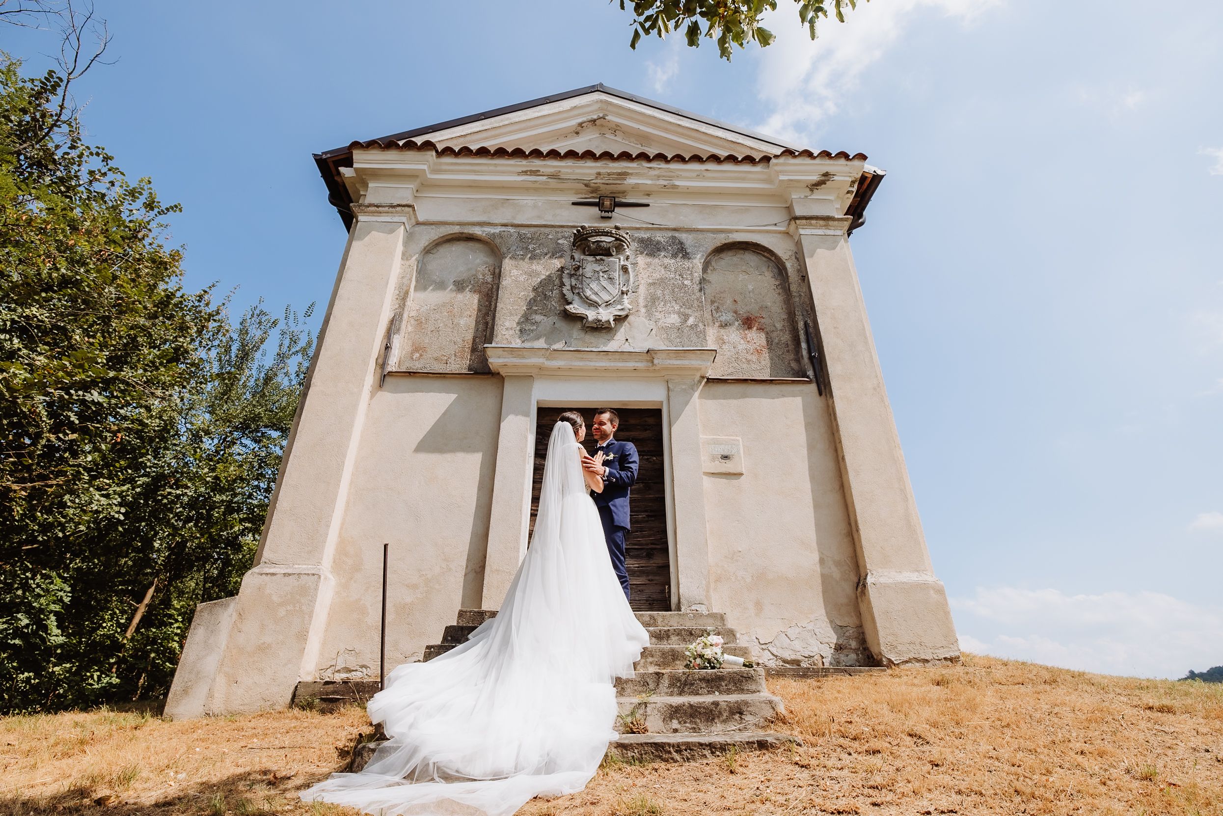 A small white chapel with a cross on top stands against a blue sky in a scenic outdoor setting.