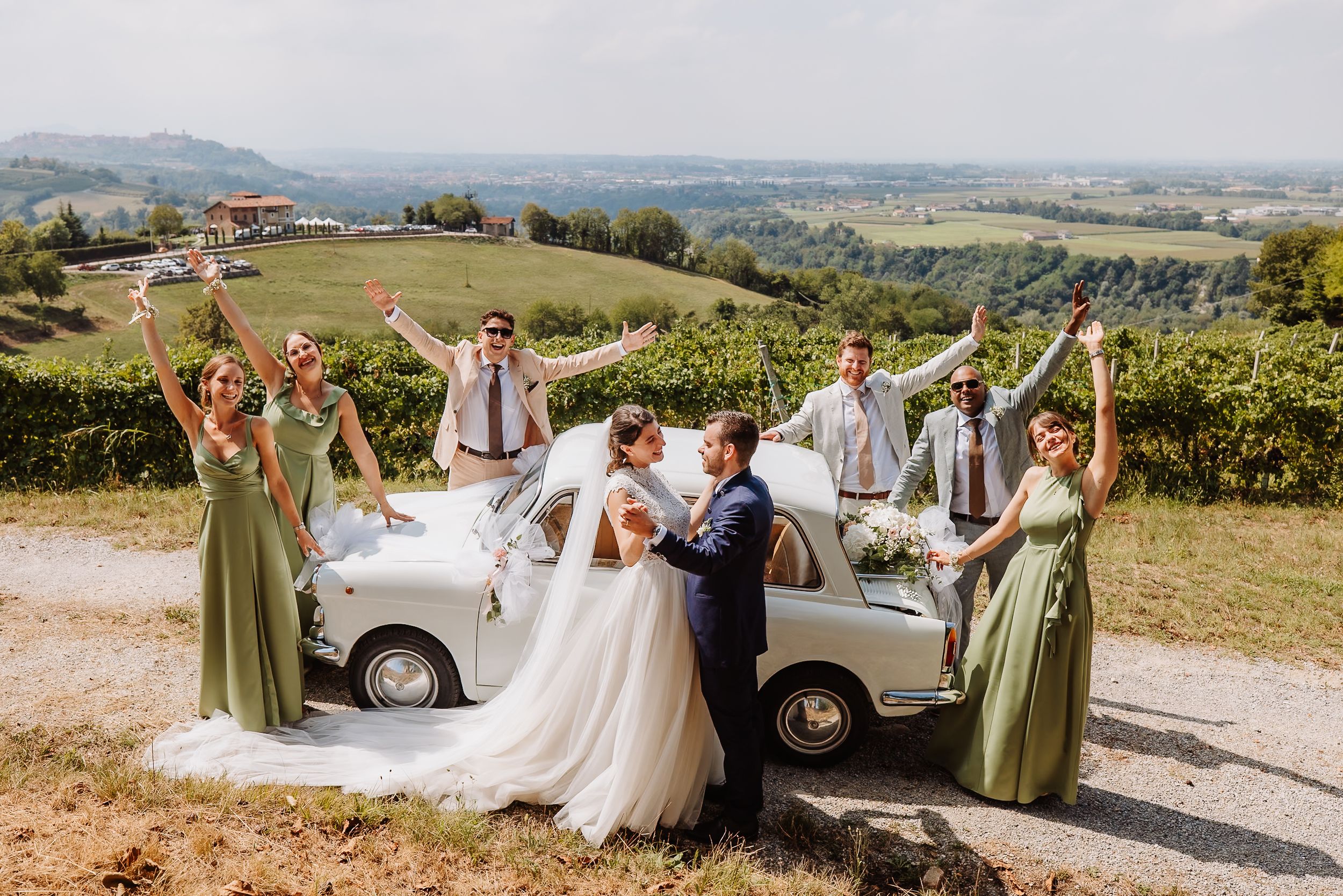 Wedding party celebrates with joyful poses against a scenic vineyard backdrop in the countryside.
