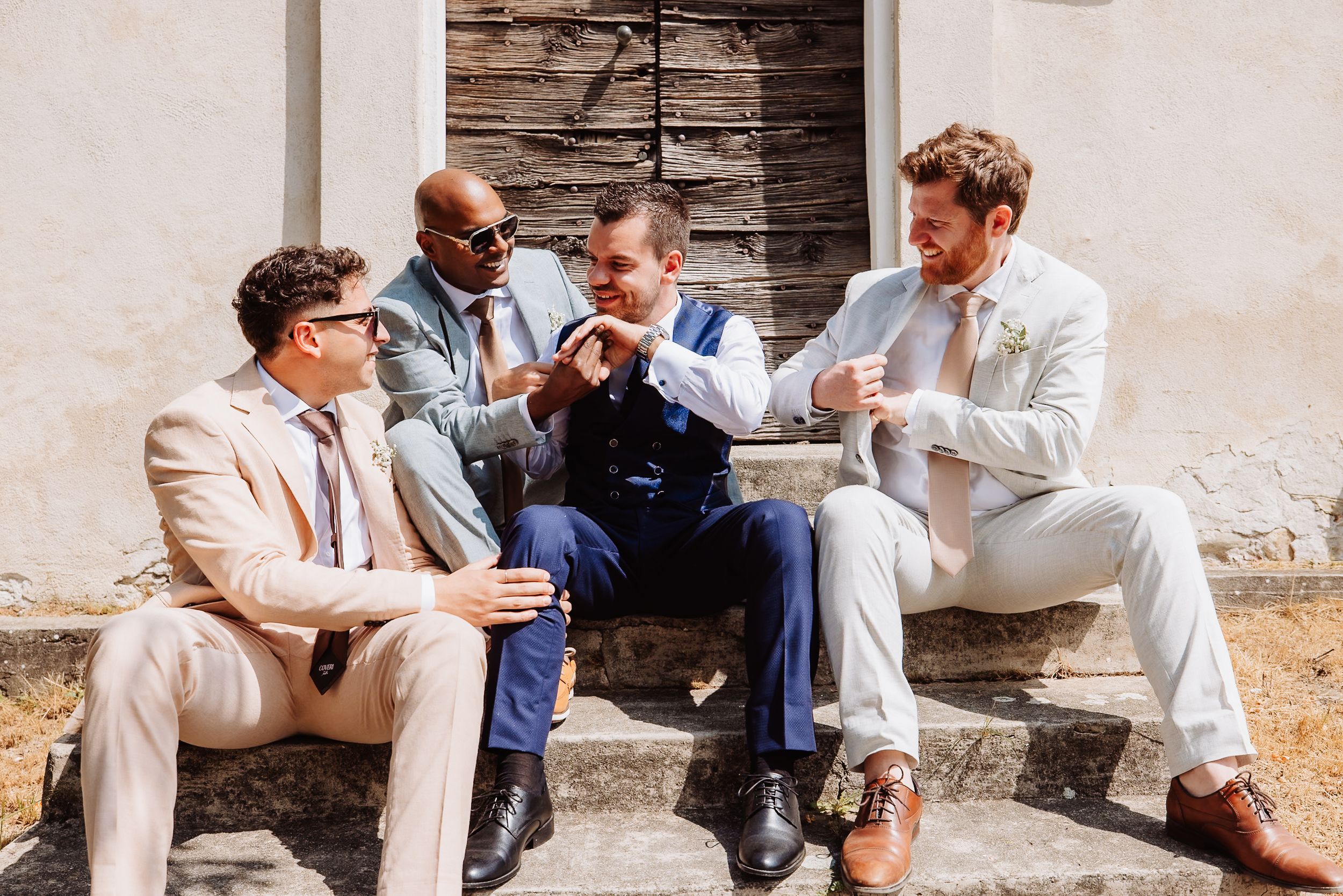 Group relaxes casually against stone wall in coordinated light-colored attire during outdoor gathering.