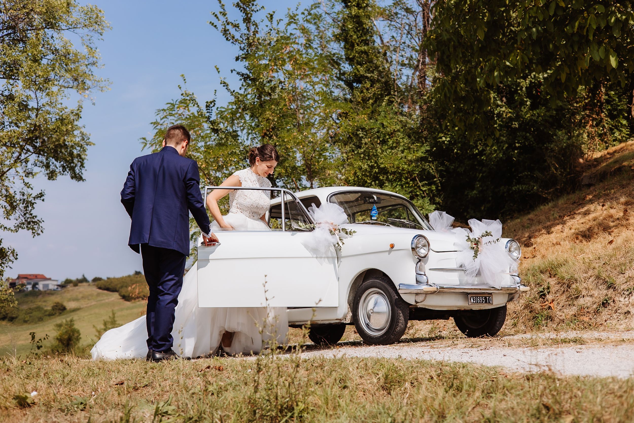 A classic white vintage car parked outdoors with autumn trees in the background.