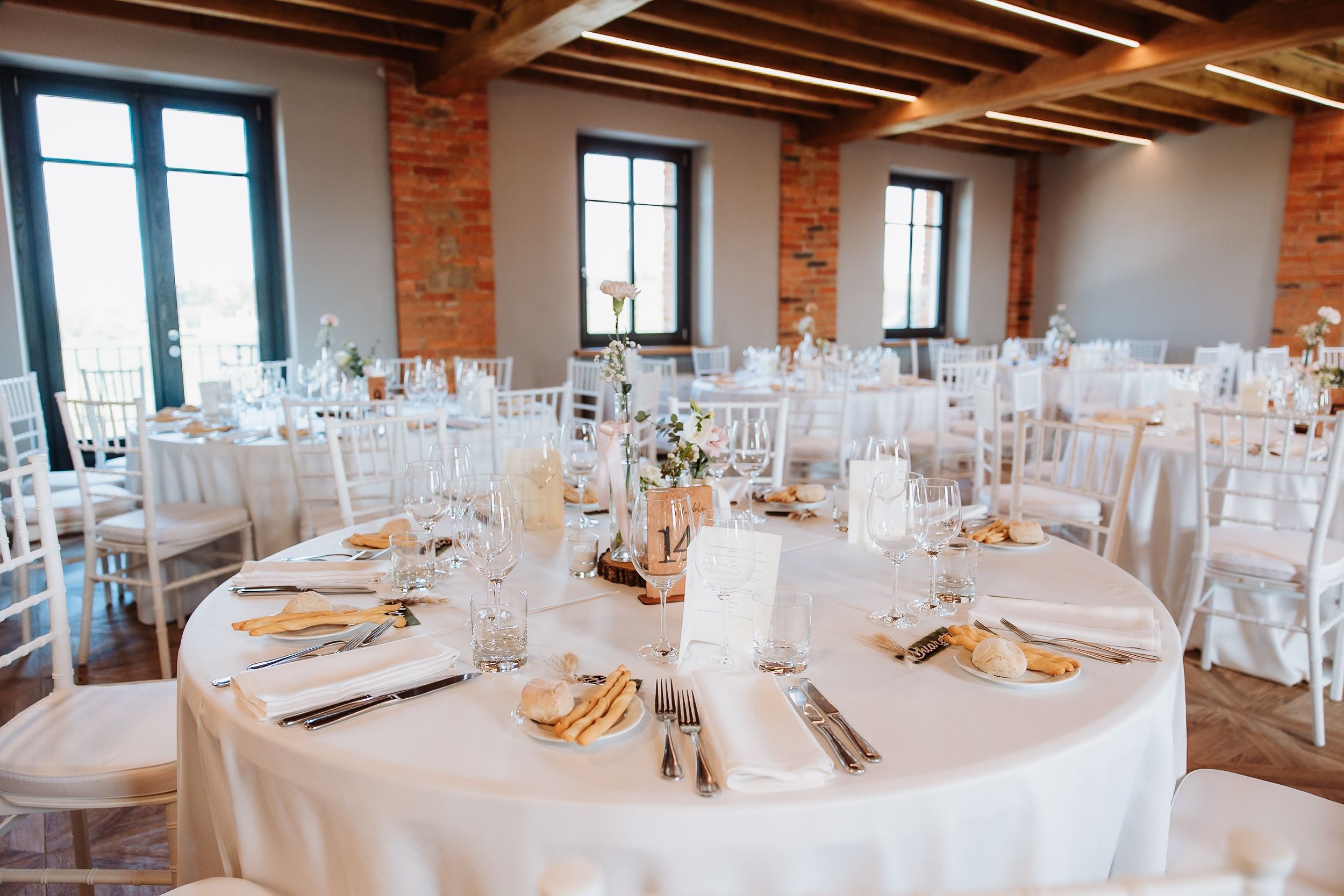 Modern industrial wedding reception venue with exposed brick walls and white table settings.