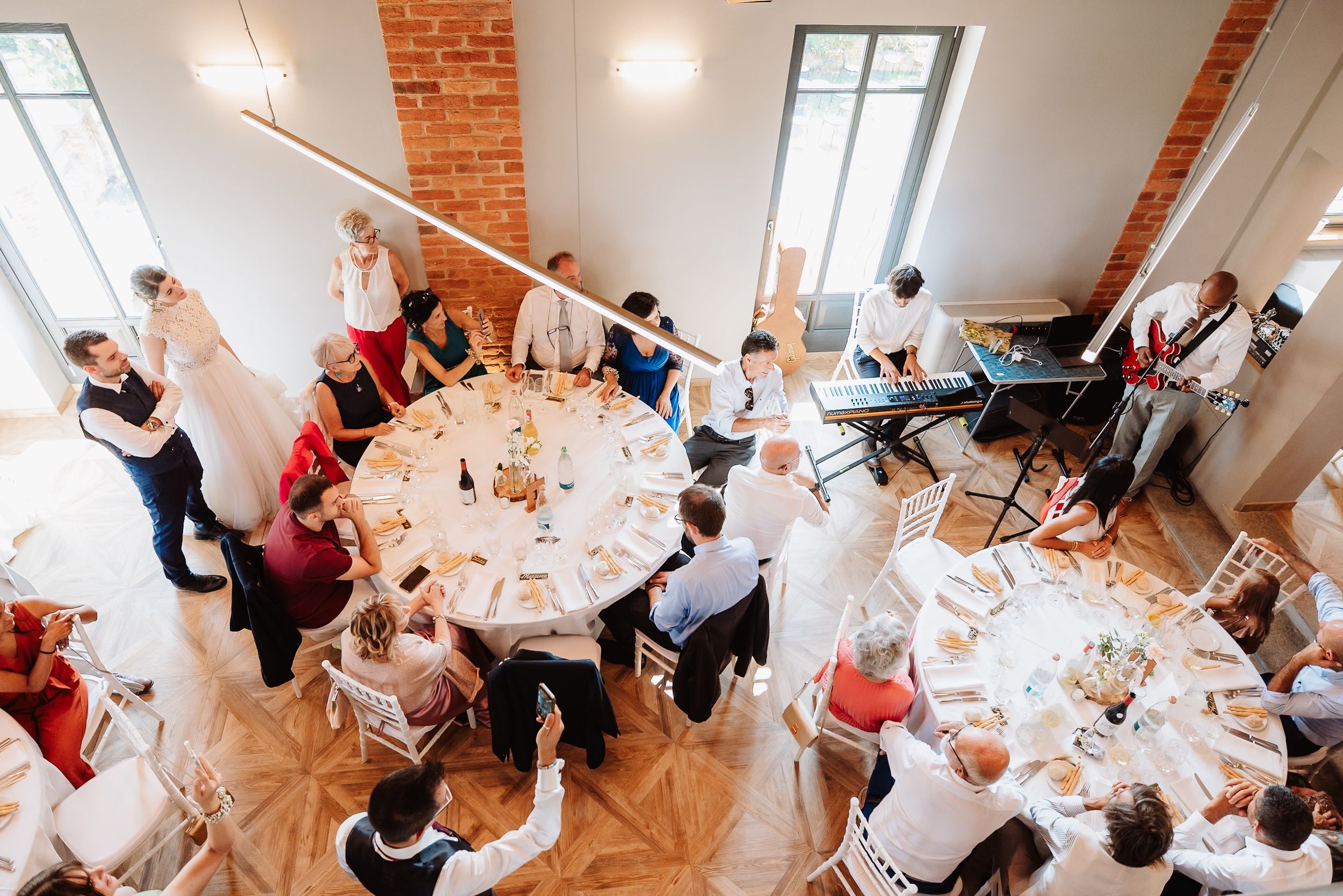 Wedding guests enjoy dinner and conversation at elegantly decorated tables in a rustic brick-walled venue.
