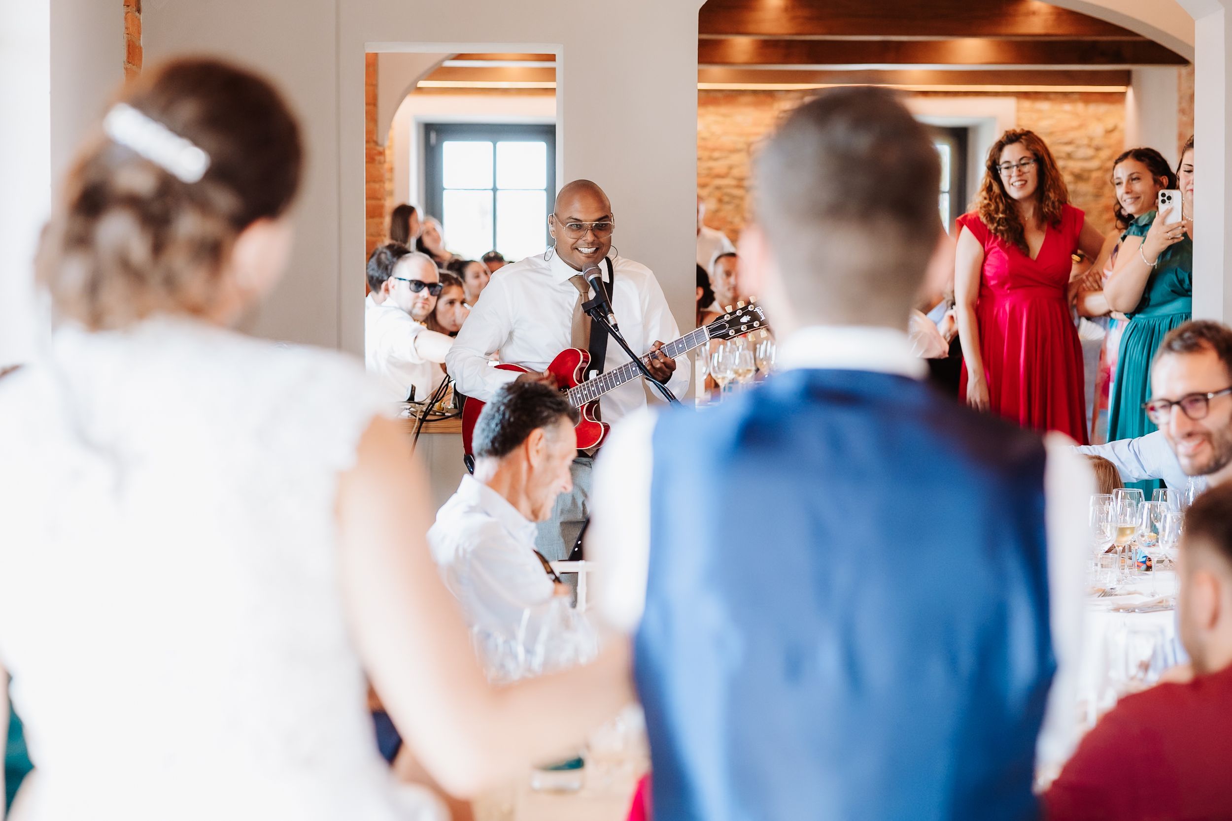 Wedding guests mingling and socializing in a rustic brick-walled reception space.