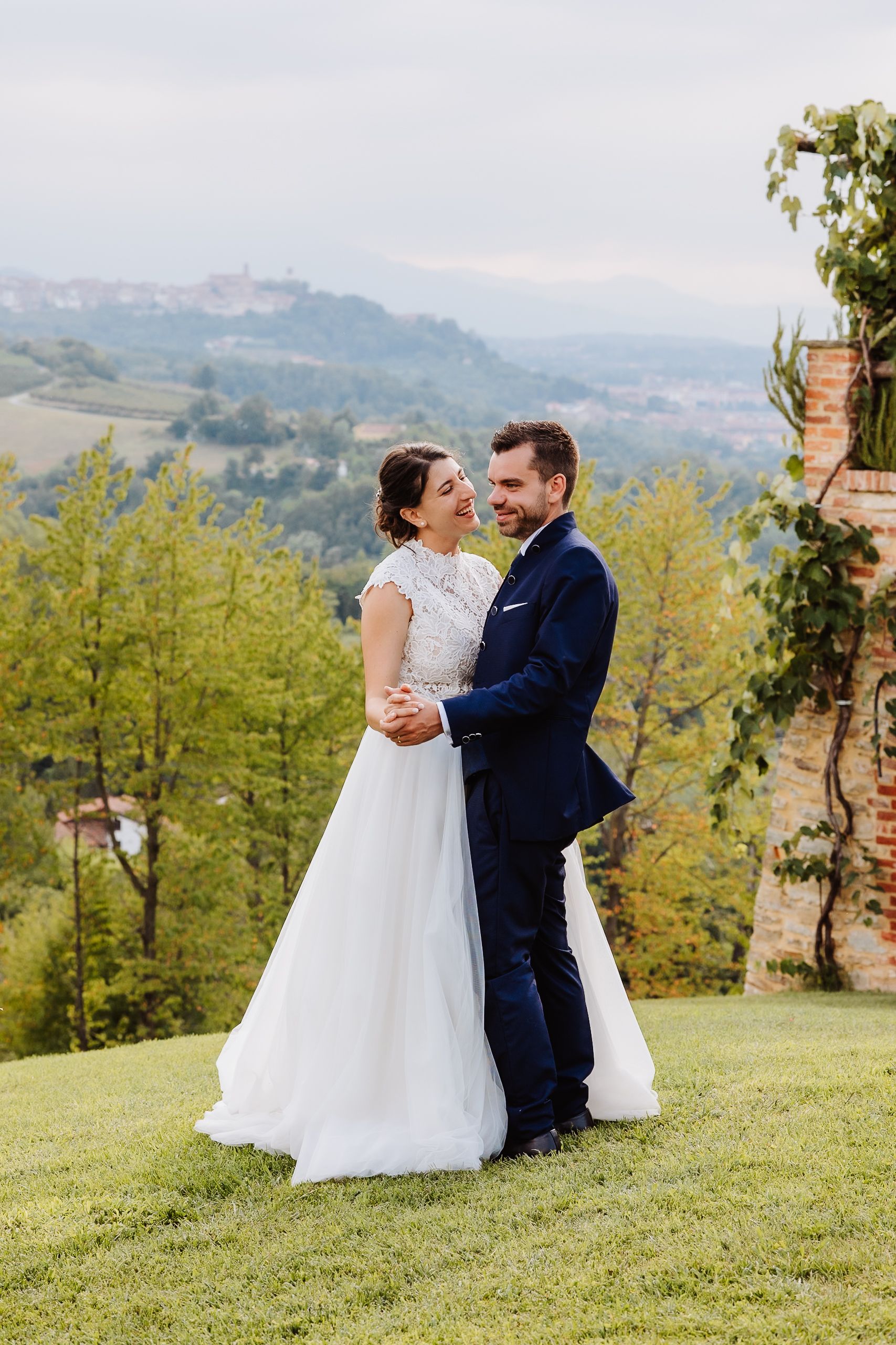 A couple in wedding attire shares a romantic moment on a hilltop with scenic mountain views in the background.