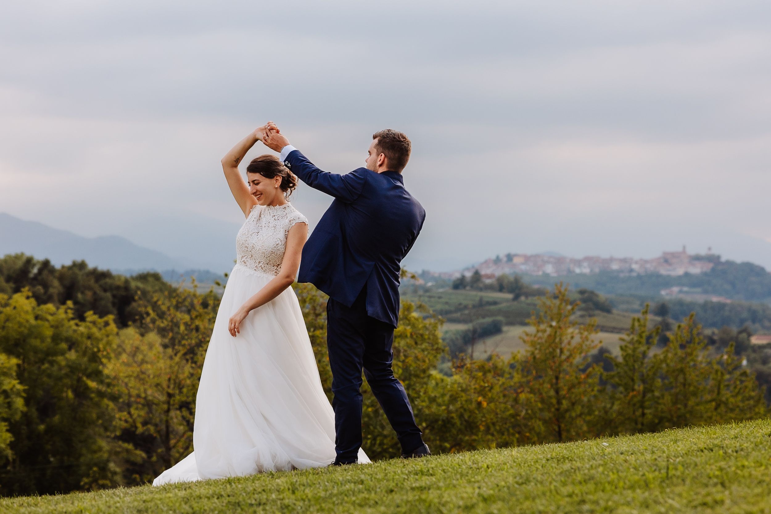 A couple embraces on a scenic hilltop overlooking a lush green landscape on their wedding day.