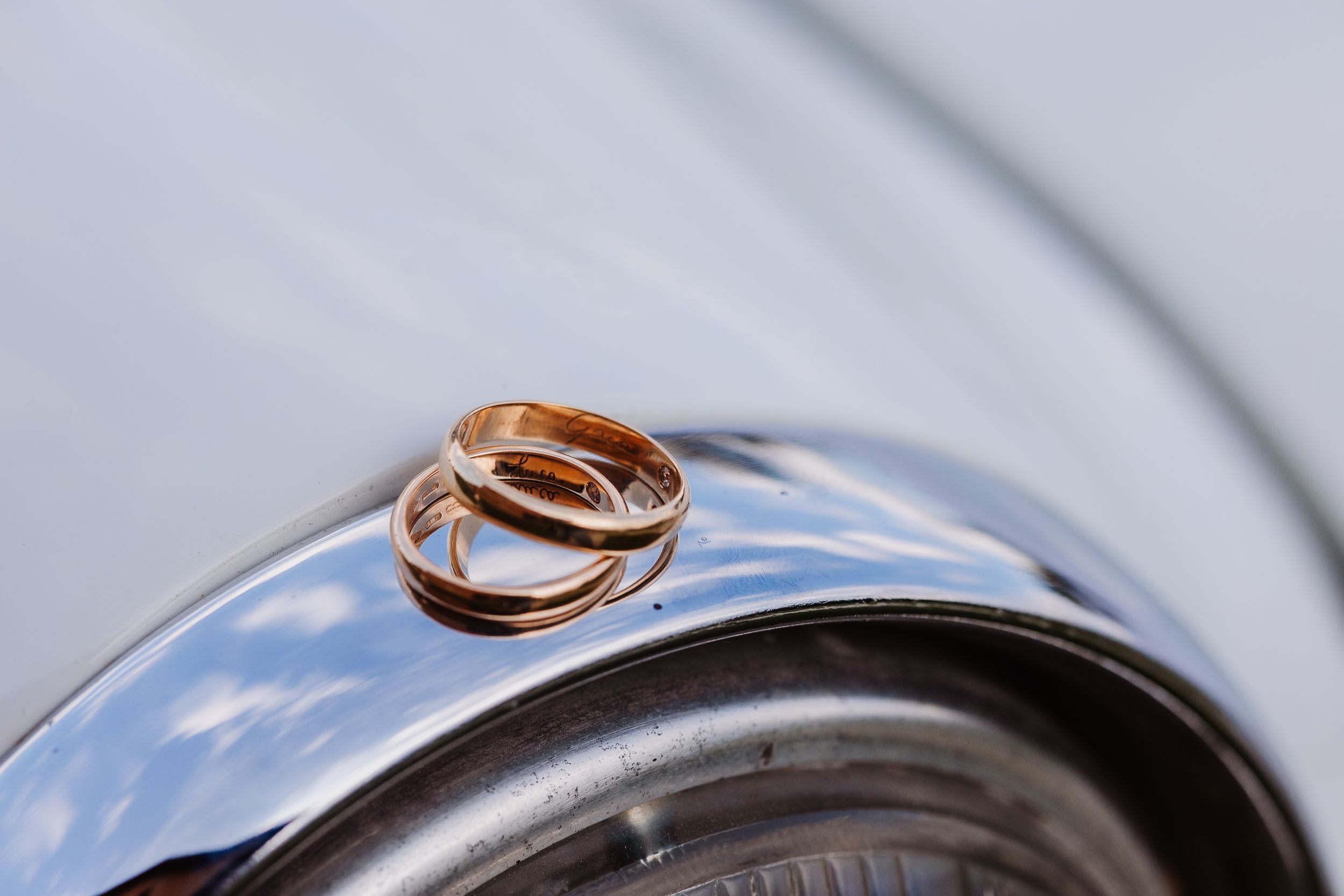 Two gold wedding rings rest on the edge of a shiny metal surface with a blurred background.