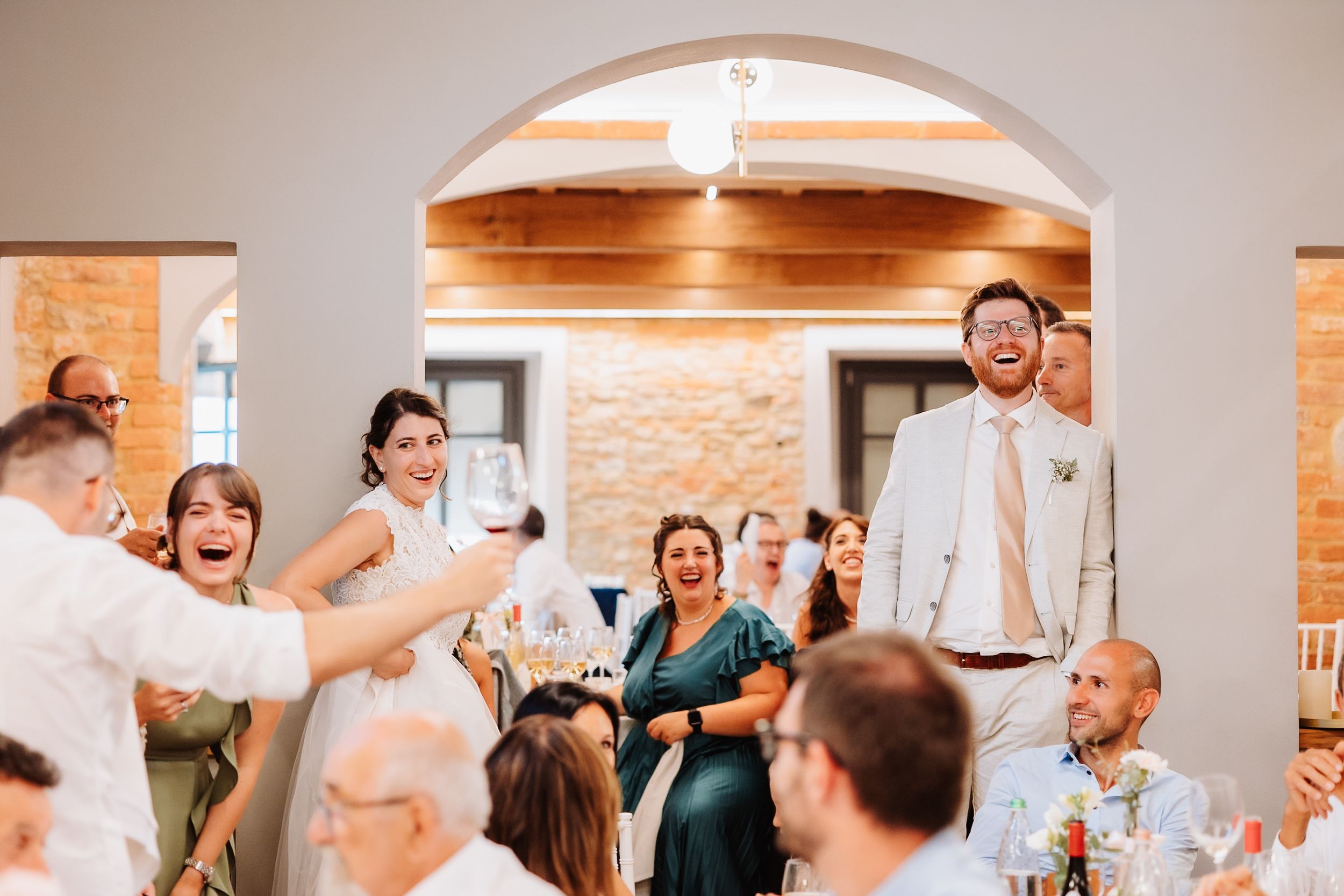Wedding guests celebrate and dance together during a joyful reception in a bright venue with brick walls.