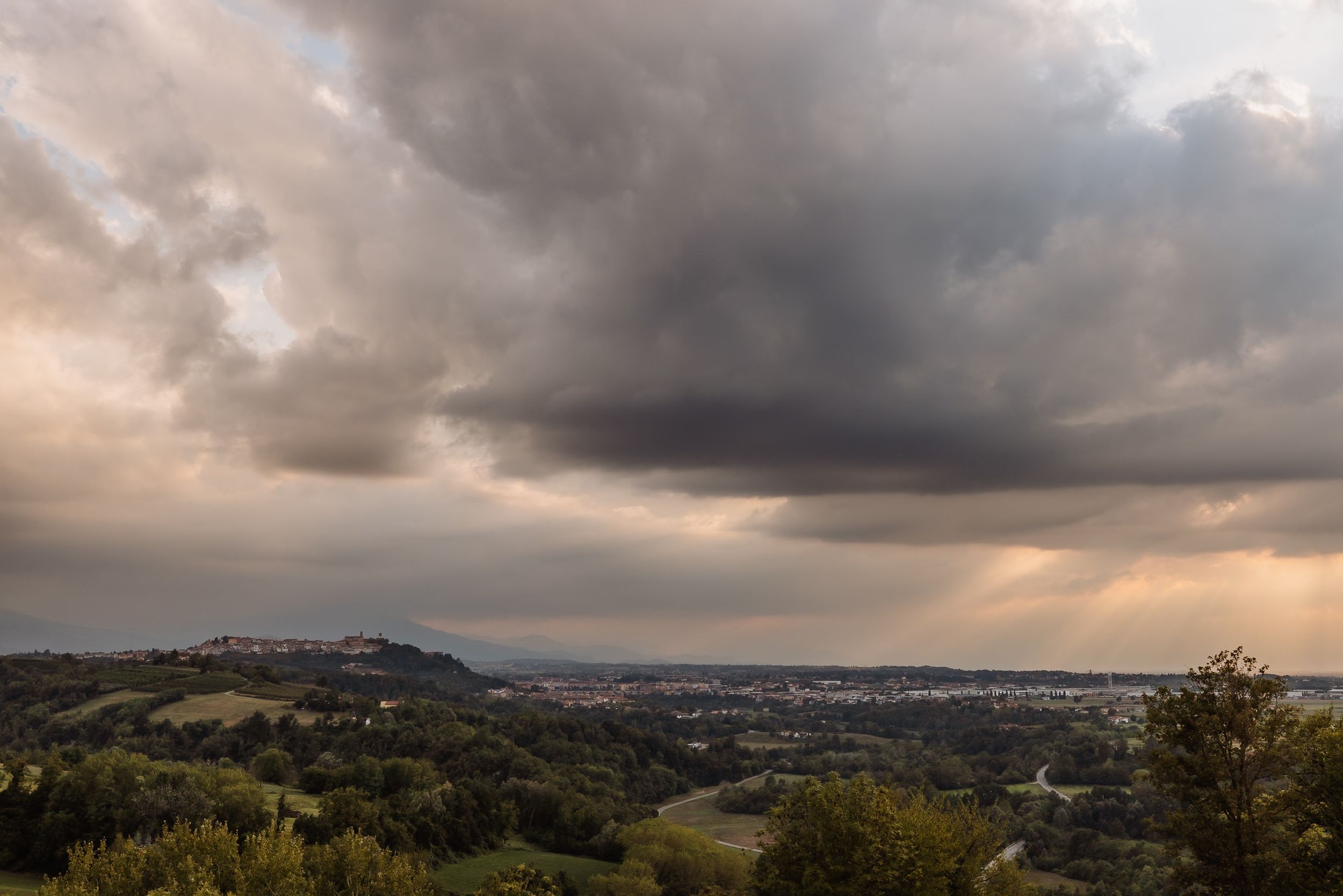 Dramatic panoramic view of storm clouds rolling over a mountainous landscape at sunset.