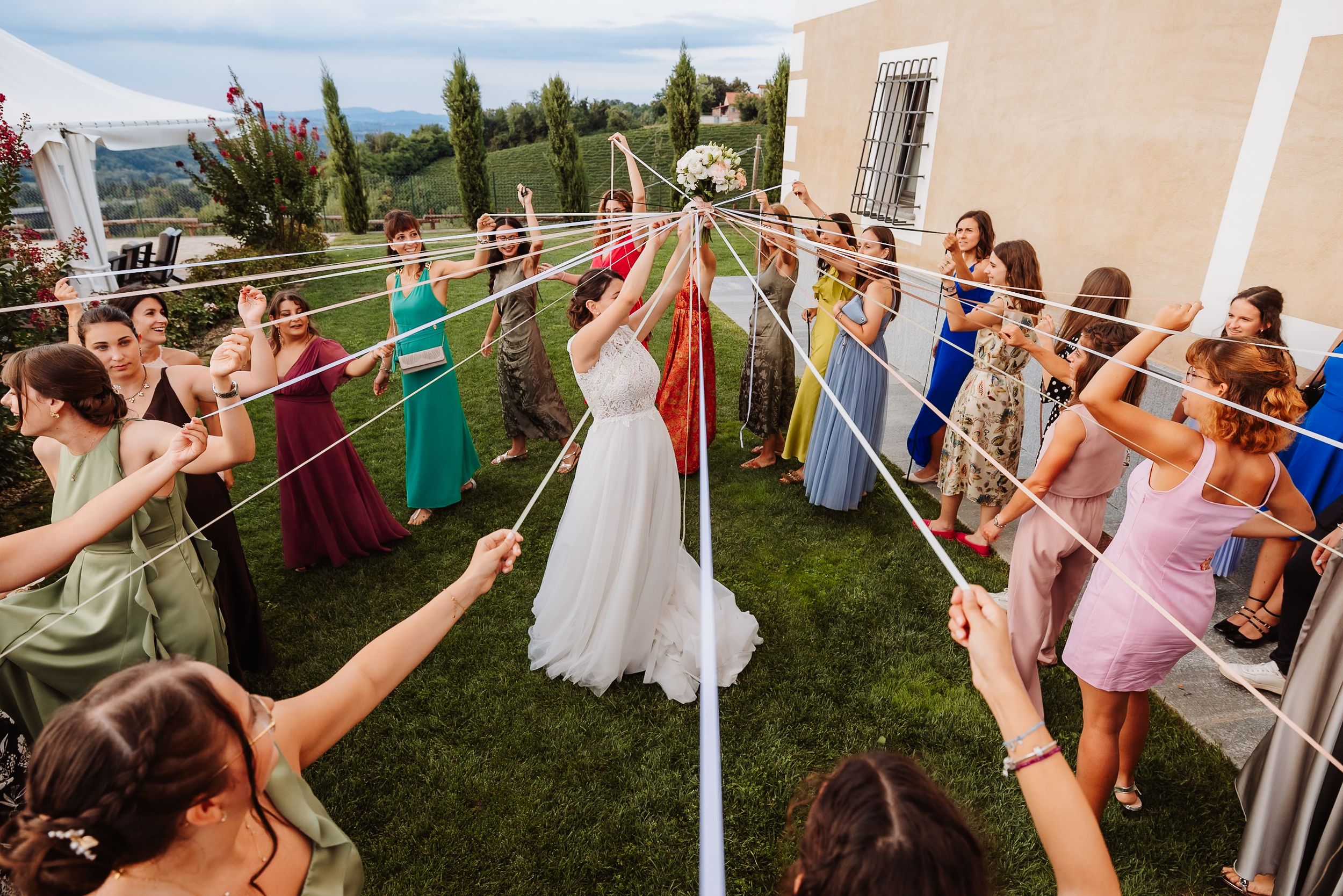 Wedding guests dance and celebrate outdoors under a string of lights during a festive reception celebration.