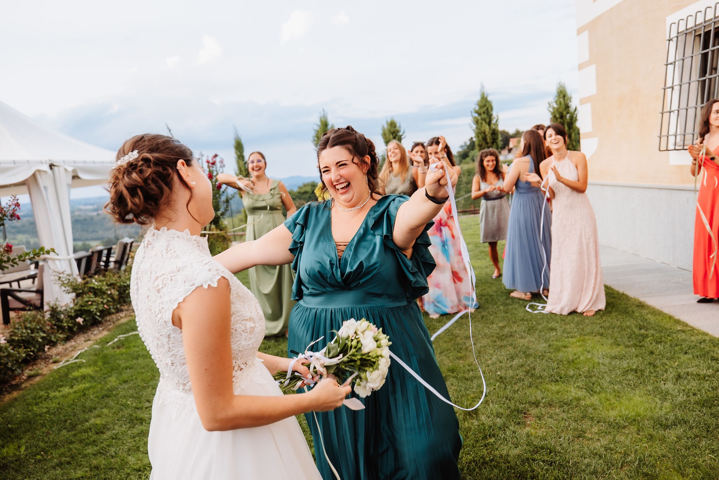 Wedding party members enjoy a celebratory toast outdoors during a sunny reception on a grassy lawn.