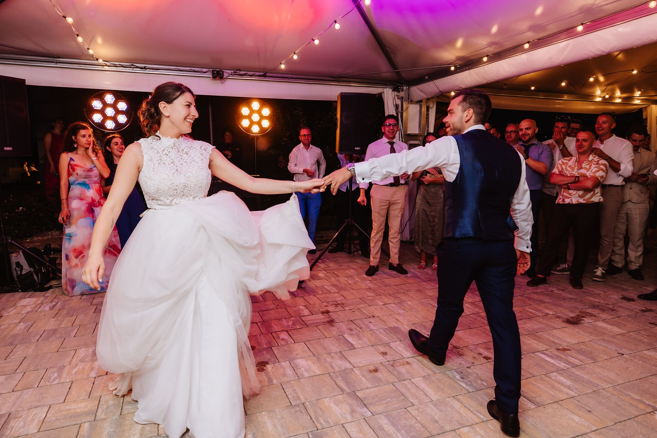 A couple performs a graceful dance spin on an illuminated ballroom floor during a wedding celebration.