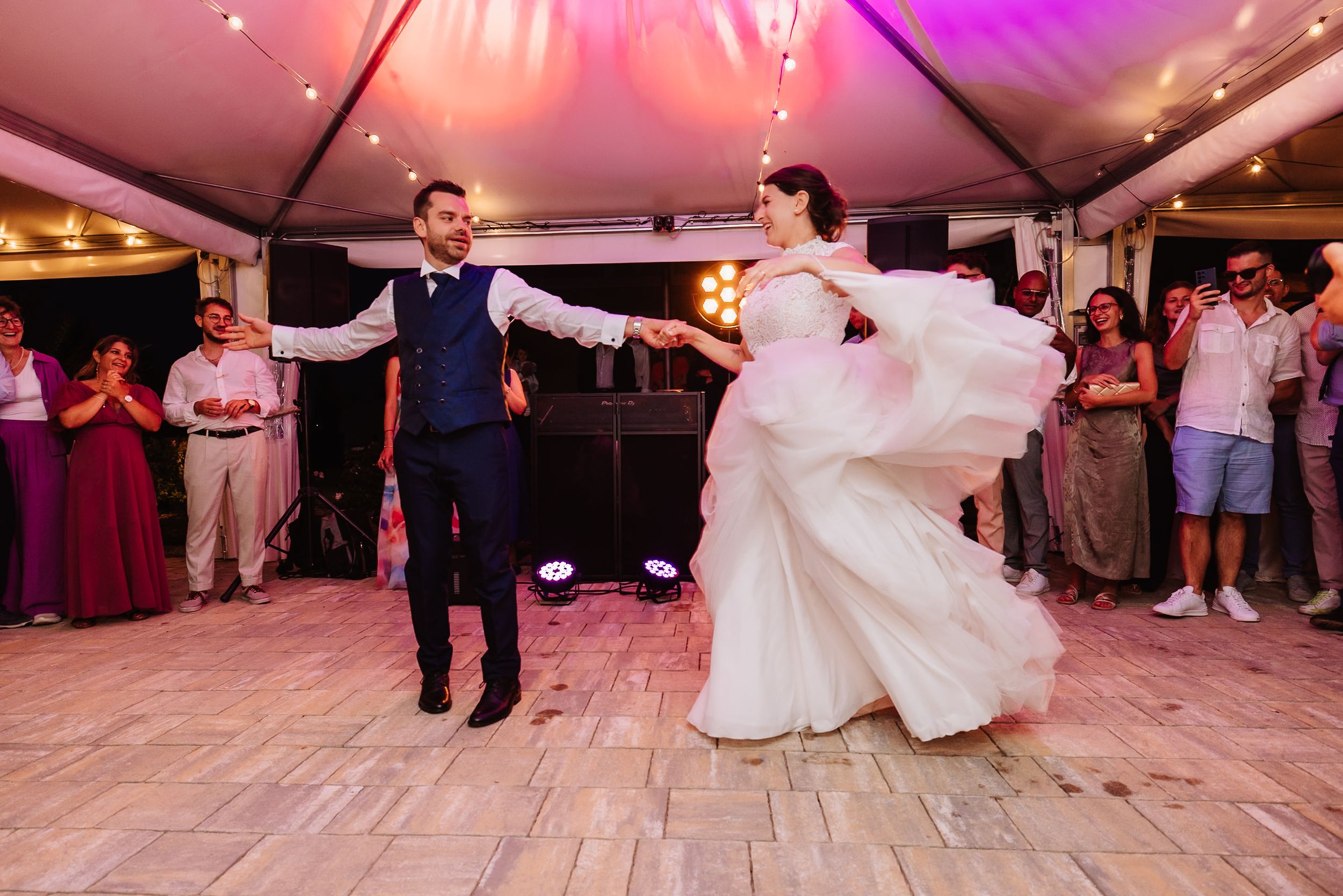 Couples dancing together at a wedding reception under purple and pink lighting on a wooden floor.