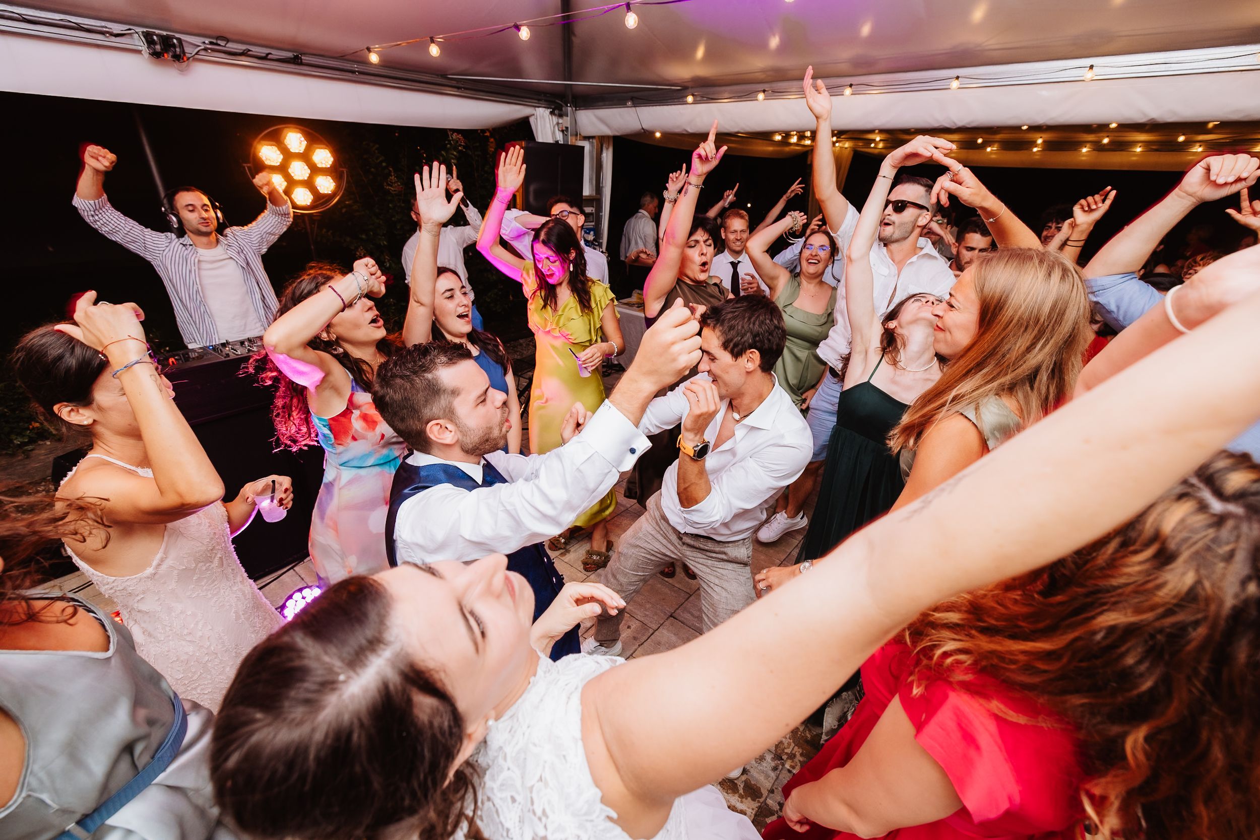 Energetic crowd dancing and celebrating with raised hands on a dance floor at a festive indoor event.