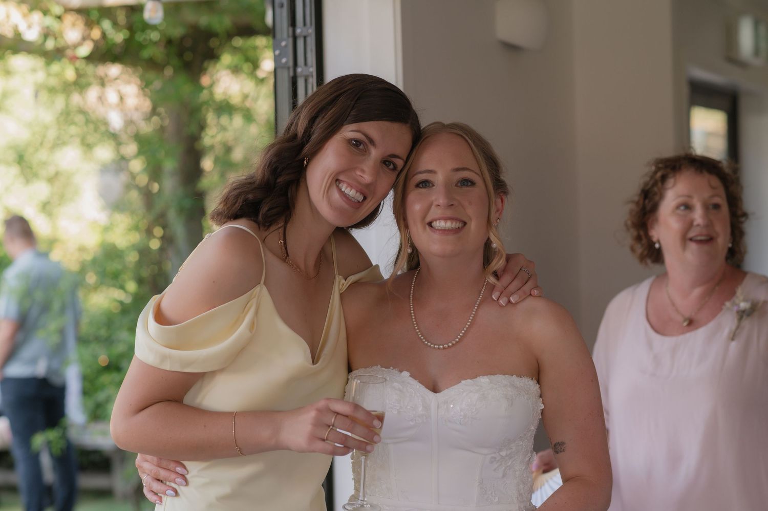 Three people share a joyful moment at a wedding celebration, with one wearing a white bridal gown.