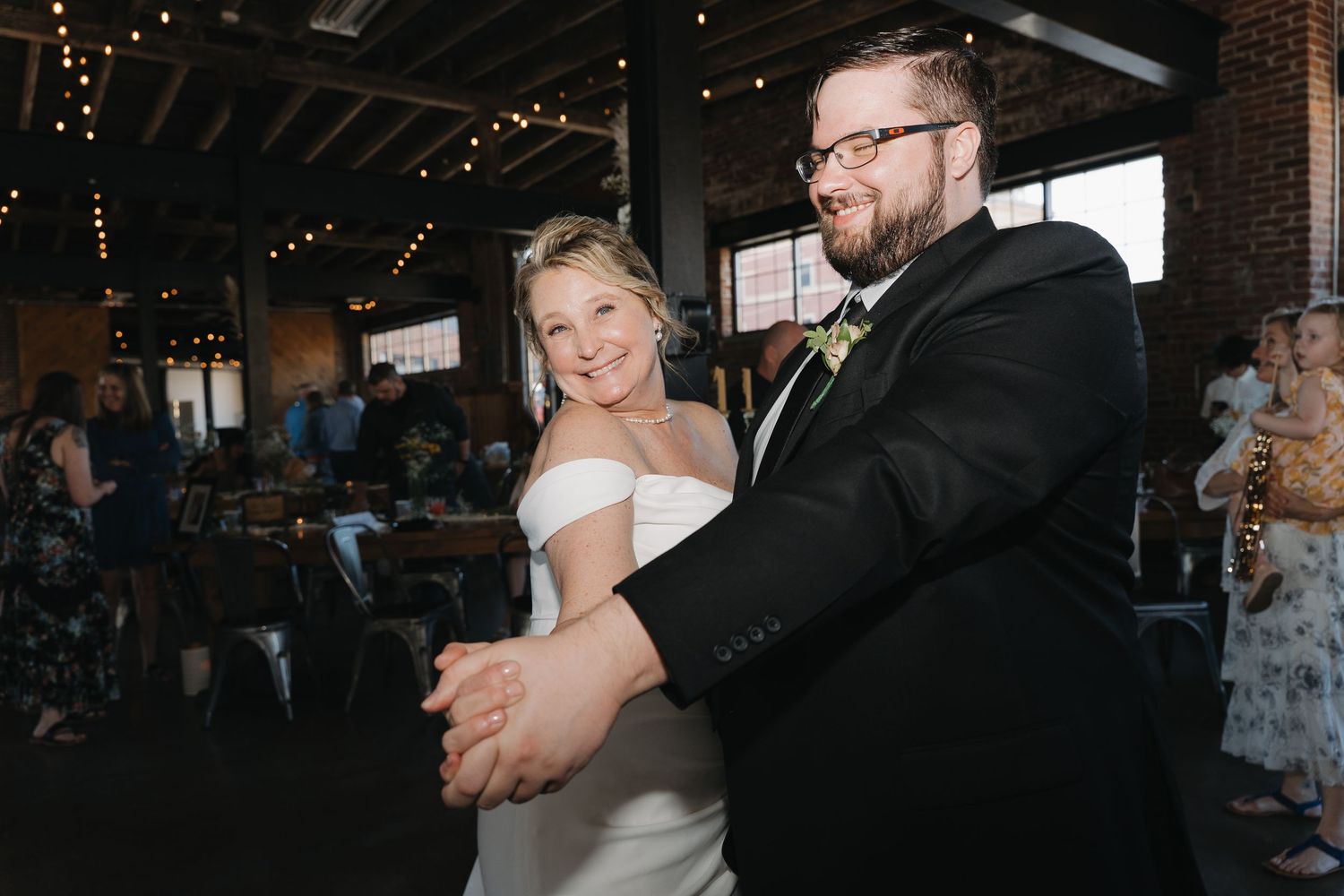 A couple dances together during their first dance at a wedding reception with twinkling lights in the background.