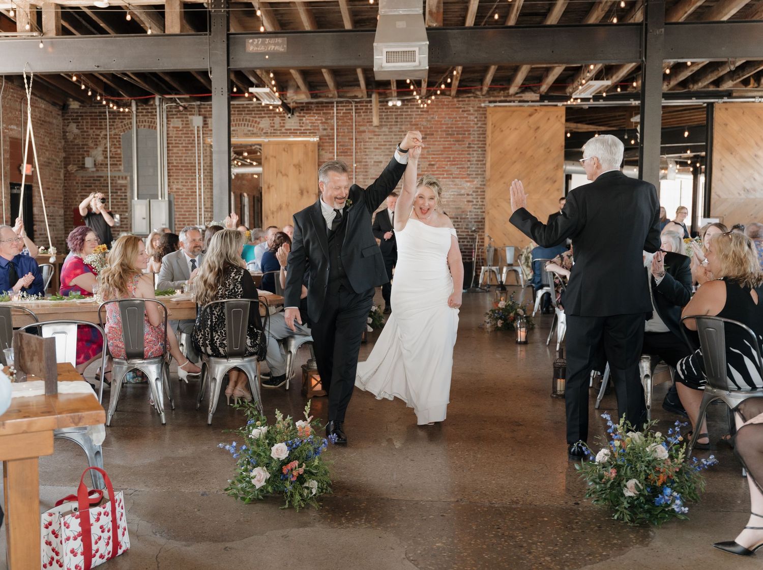 A panoramic view of a rustic barn wedding reception with wooden beams, string lights and floral decorations.