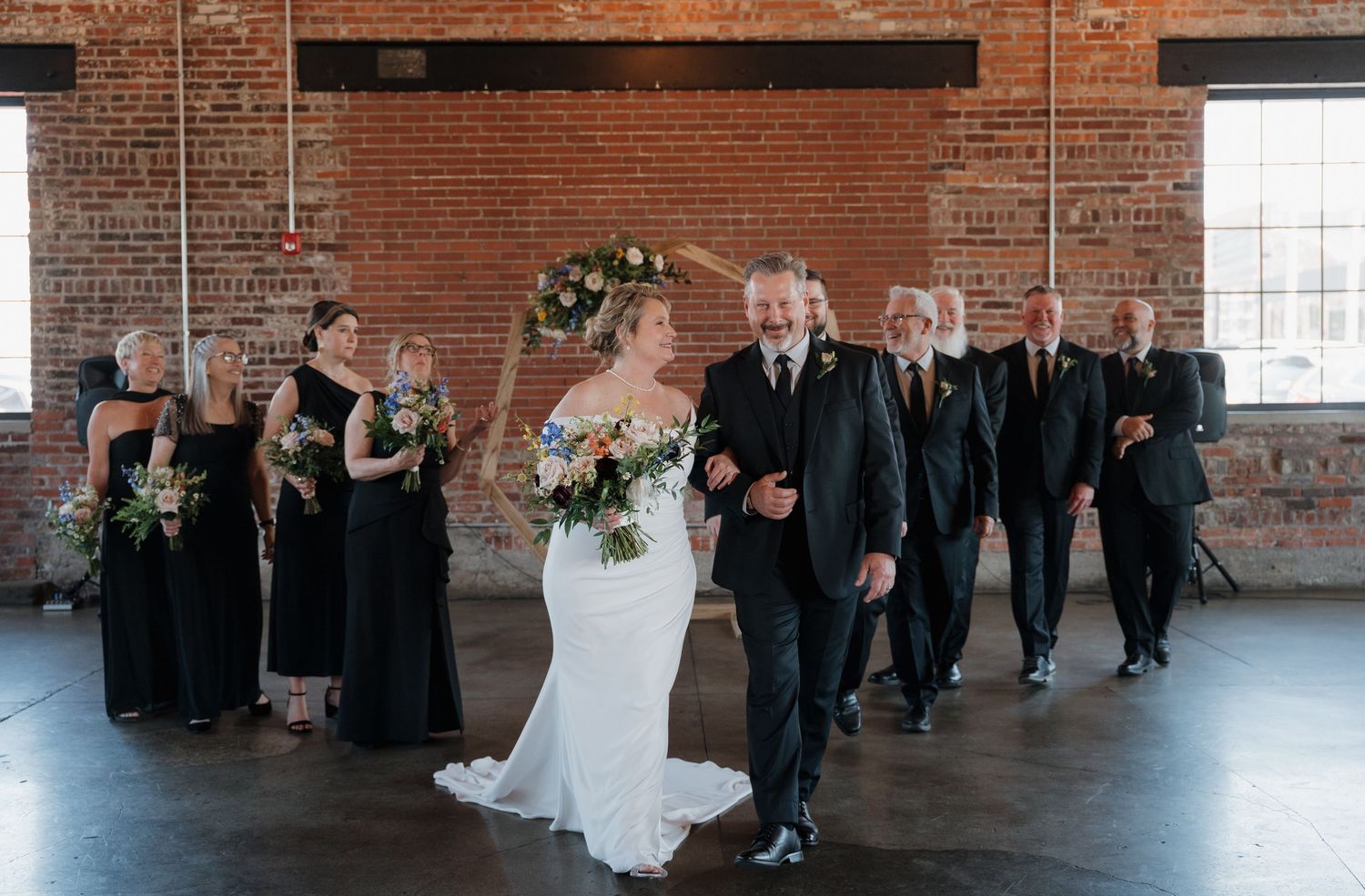 Wedding party poses together in rustic brick venue with industrial windows and natural light.