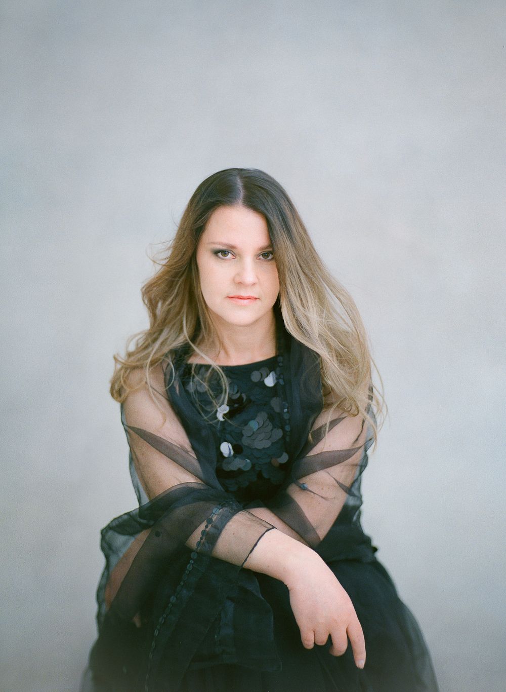 Studio portrait in black lace dress with sheer sleeves against grey background.
