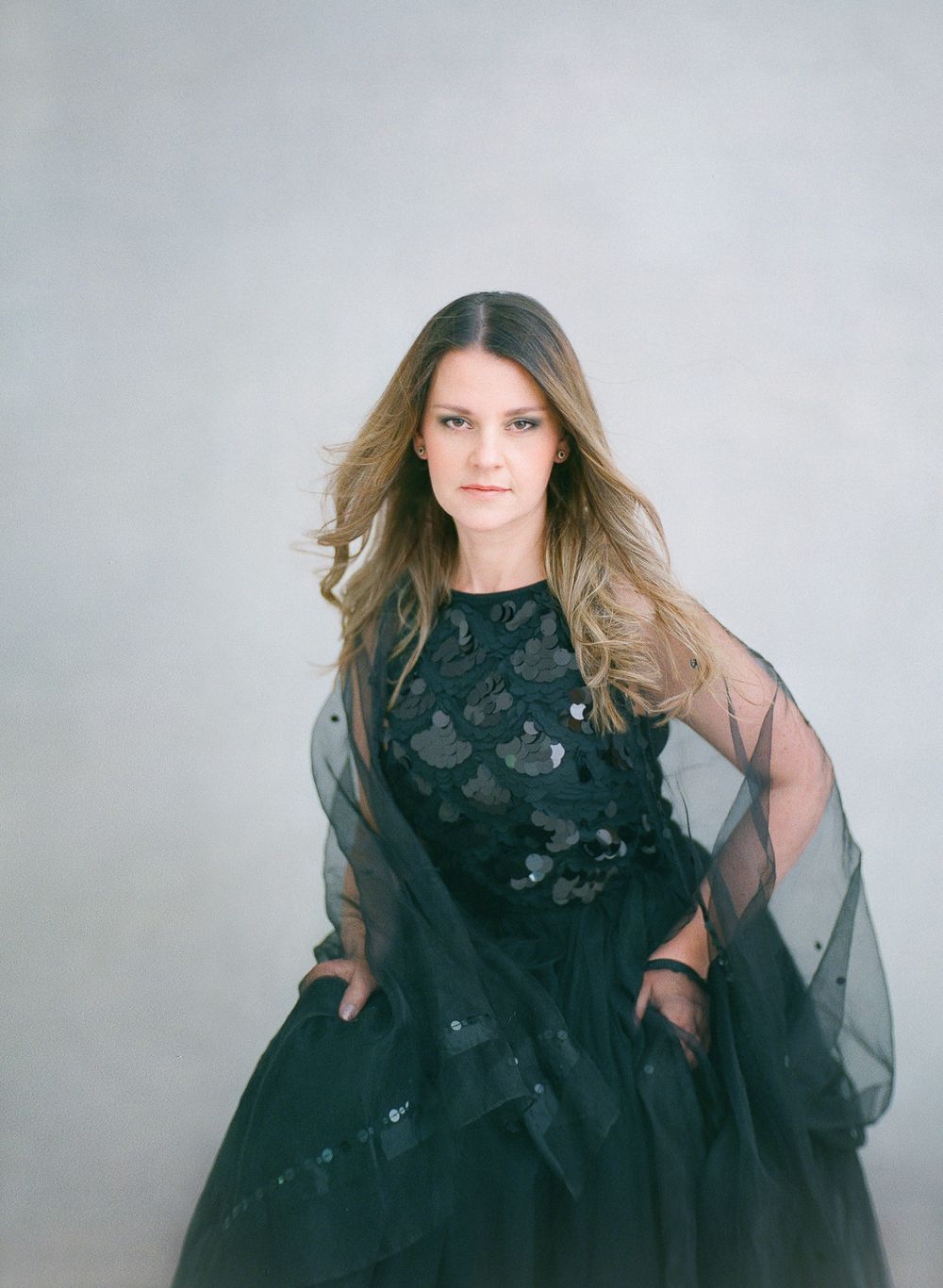 Fashion model wearing black tulle gown with sheer overlay in studio setting.