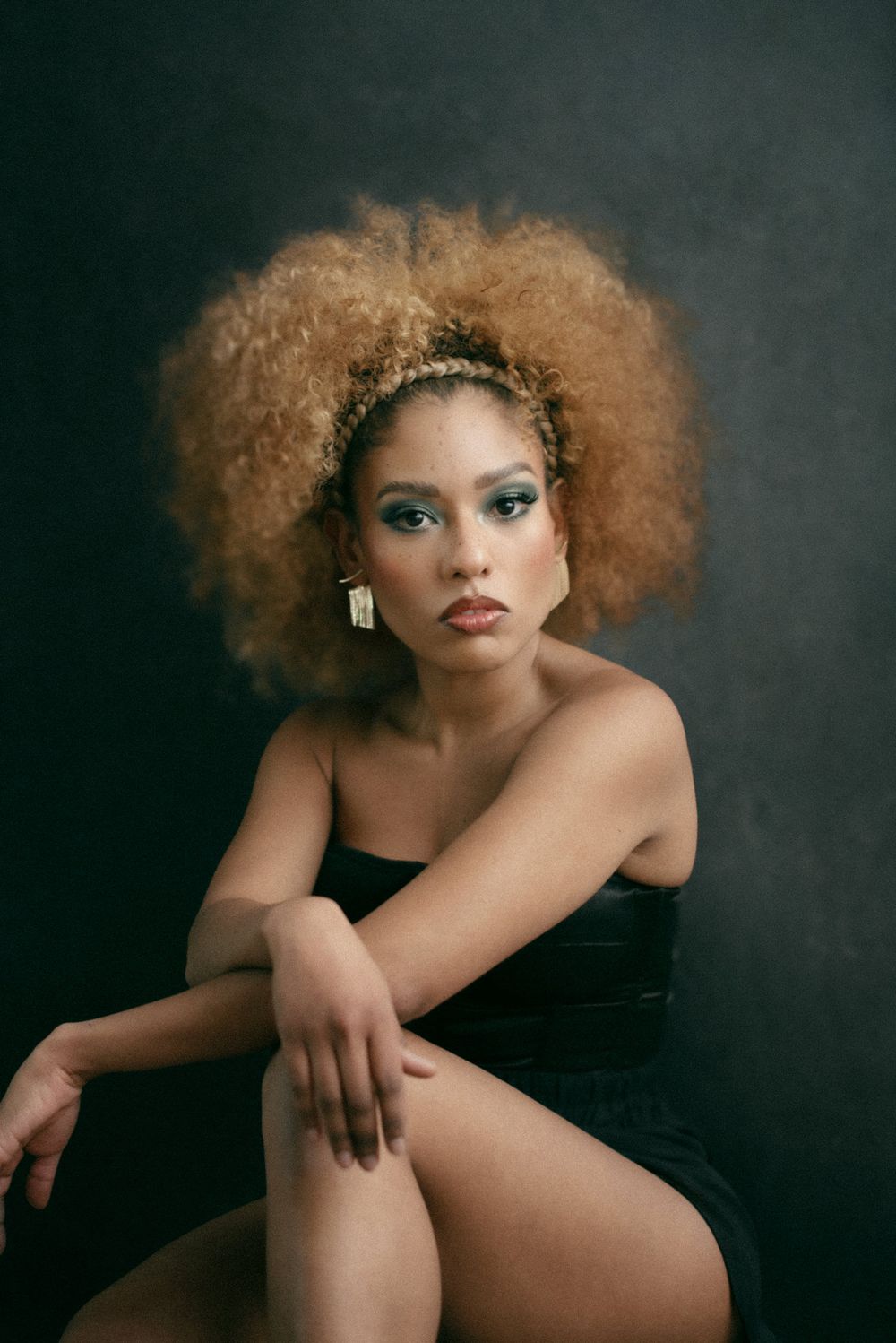 Studio portrait with natural afro hair, headpiece and black dress against dark background.