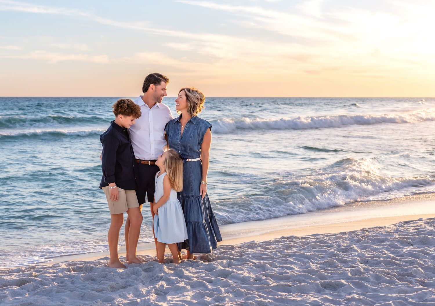 Family enjoying a beautiful sunset together on a white sandy beach with gentle waves rolling in.