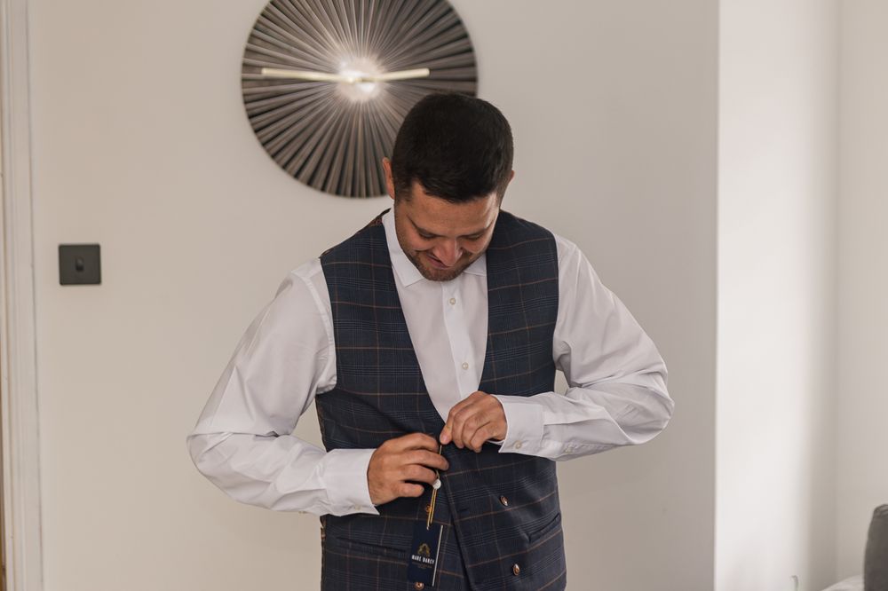 Man in formal attire adjusting his cuffs in a modern interior setting.