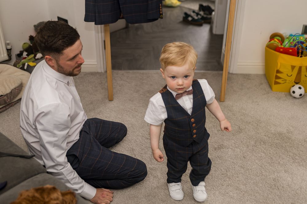 A small child in formal wear plays on a carpeted floor with toys visible in the background.