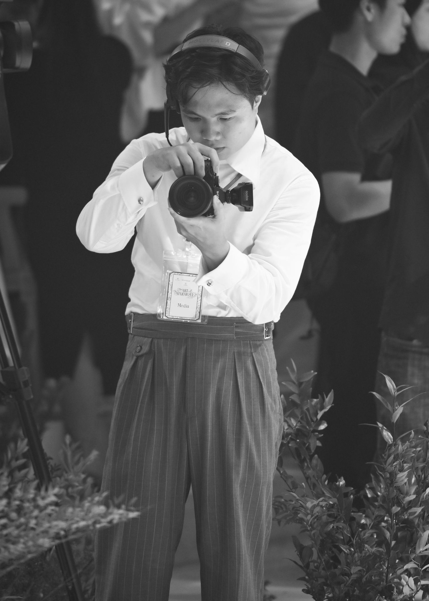 Young boy in white shirt and bow tie photographing with camera at outdoor event, black and white.