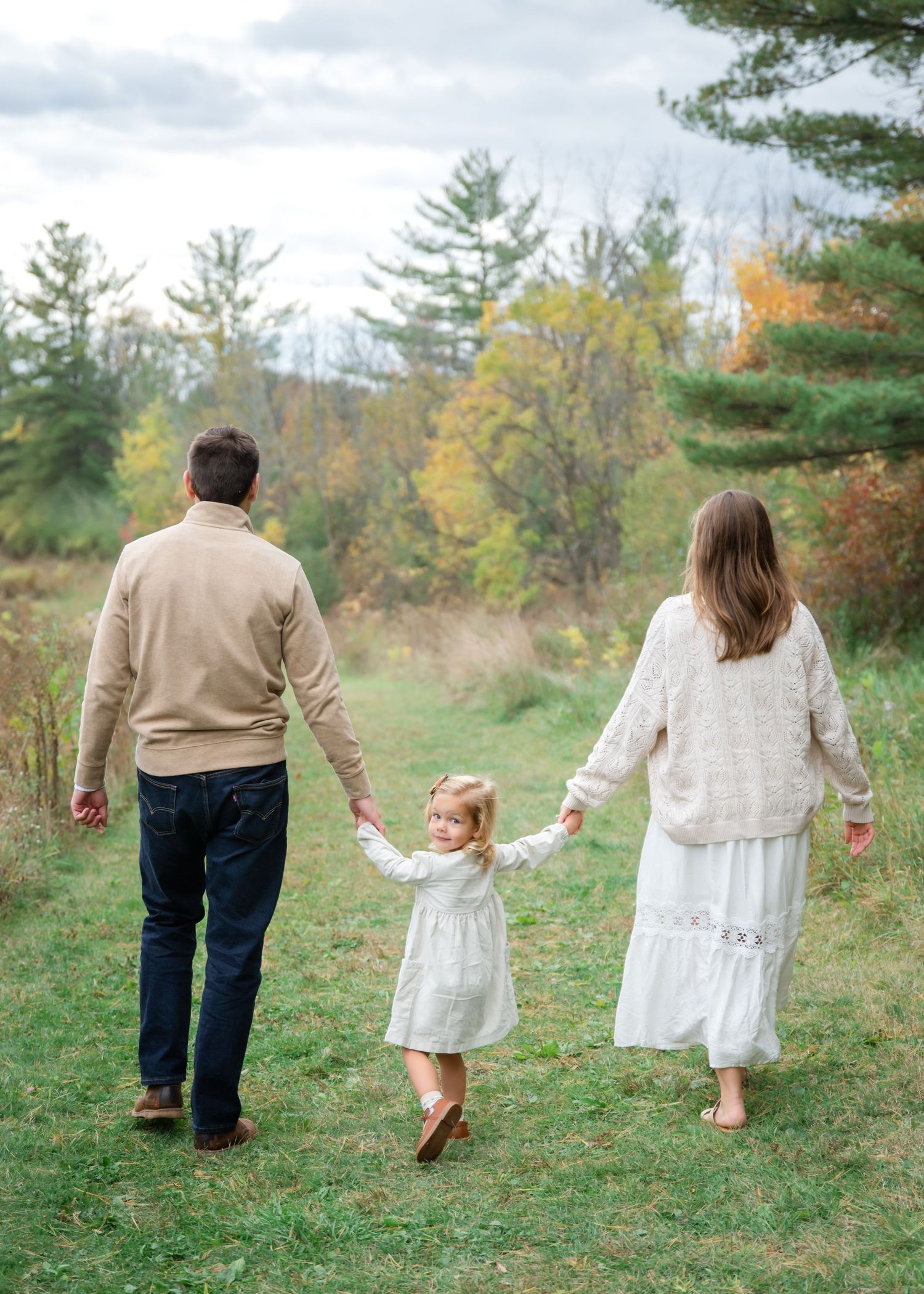Family wearing coordinated beige and white outfits poses together among autumn trees and fallen leaves.