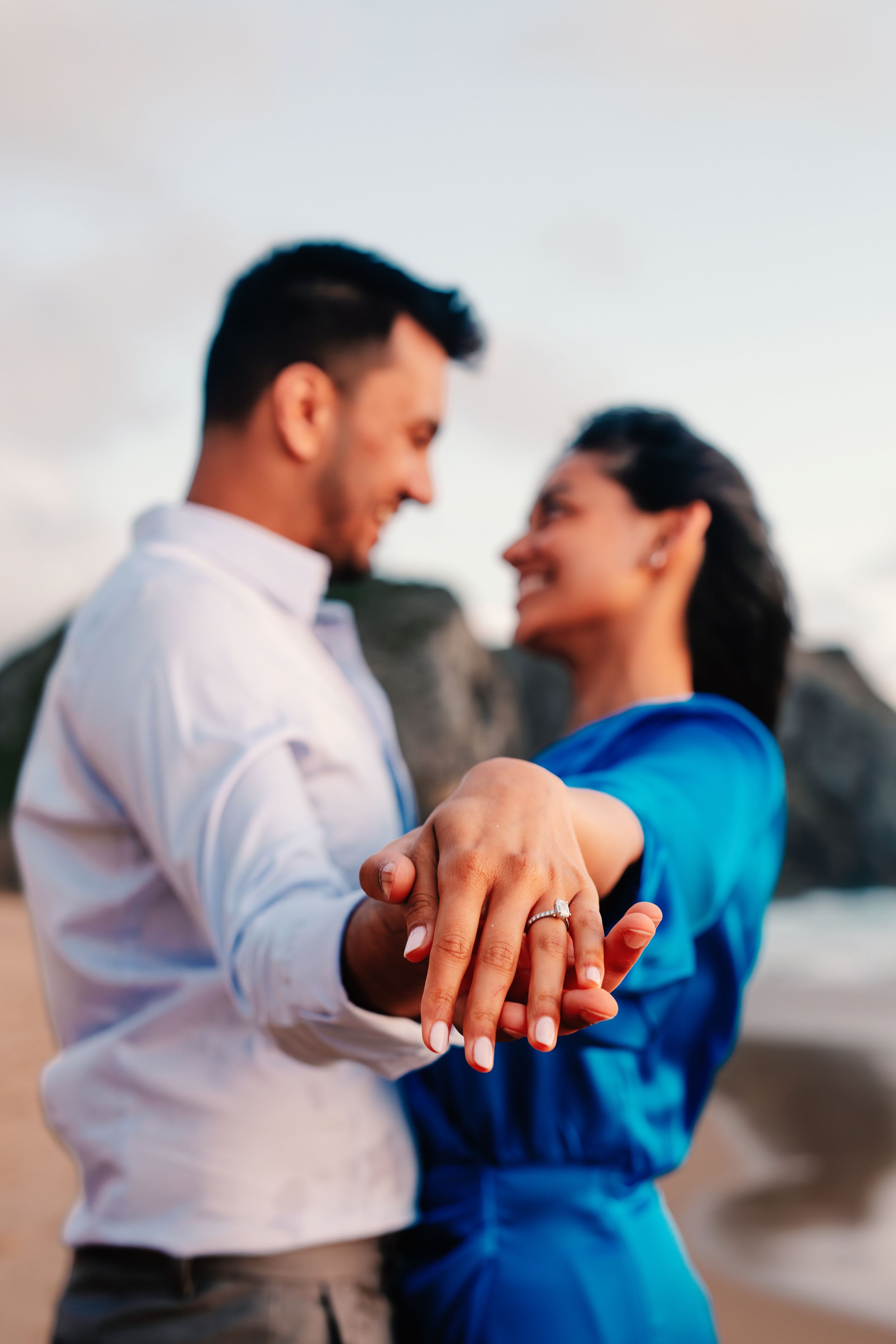 A romantic couple in white and blue outfits hold hands on the beach at sunset, shown in a series of connected photos.