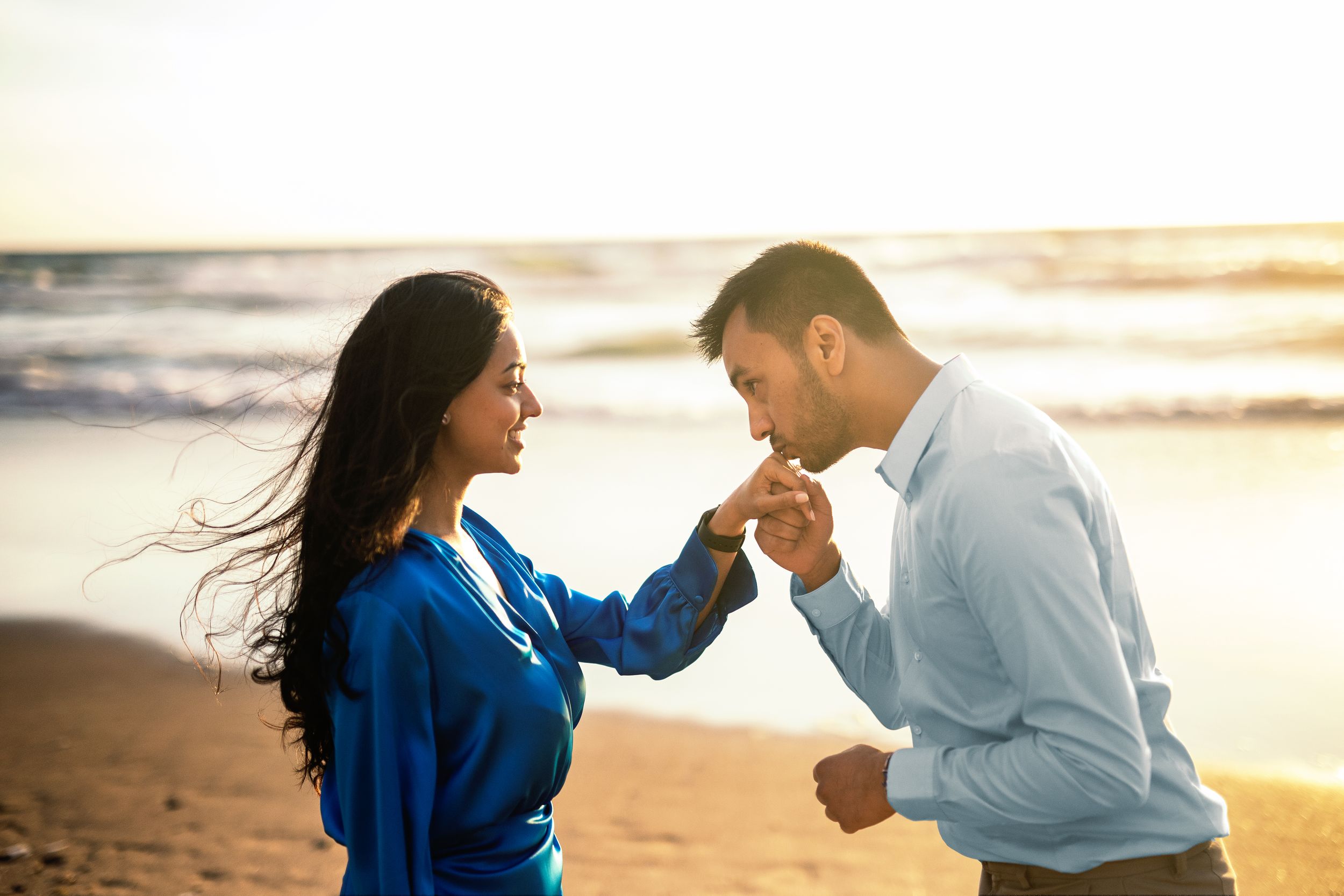 Couple shares romantic moments during golden hour photoshoot at the beach in matching blue and white outfits.