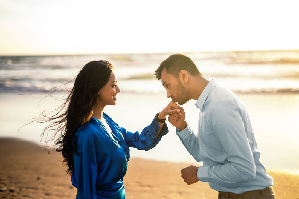 Couple shares romantic moments during golden hour photoshoot at the beach in matching blue and white outfits.