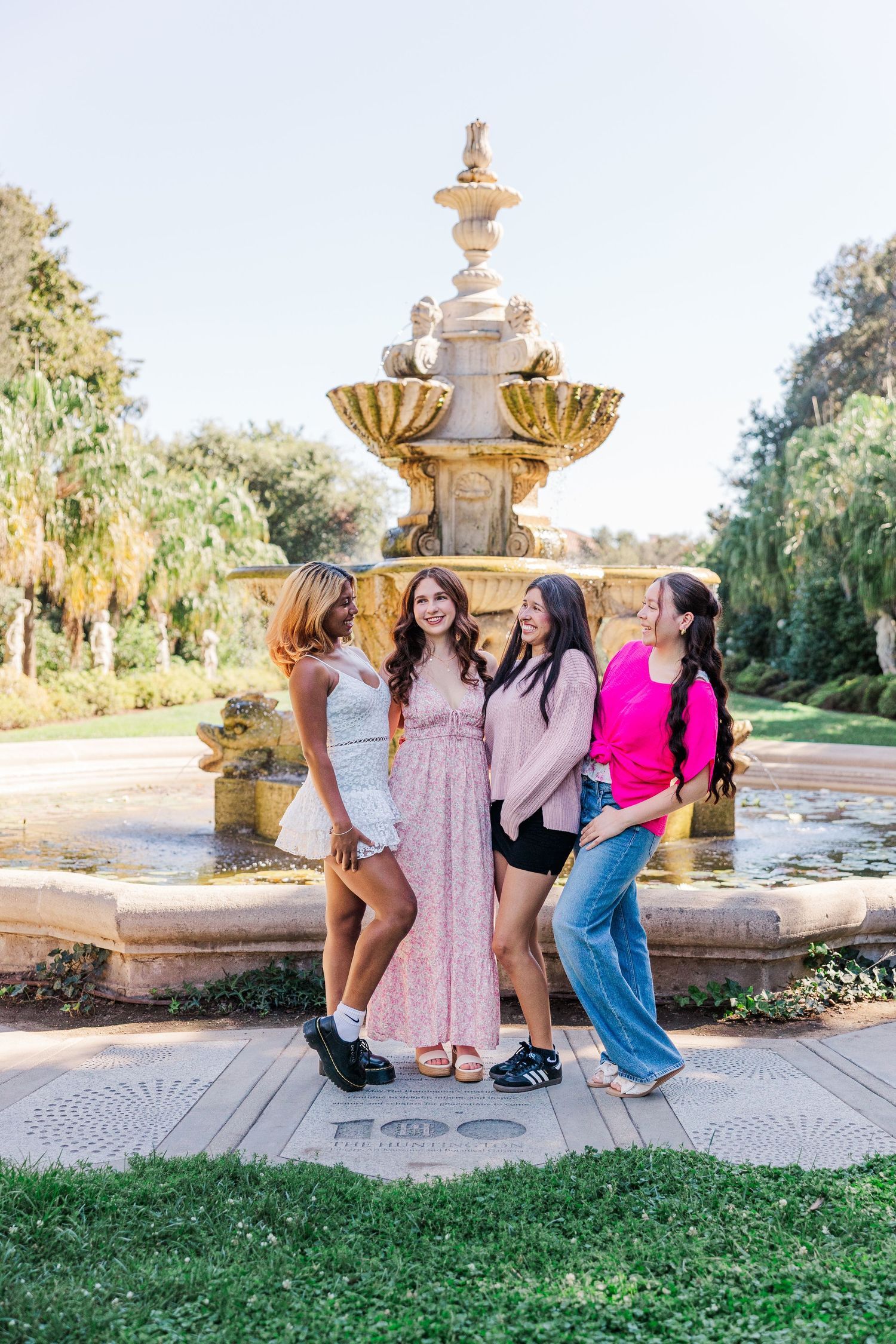 Group poses together in front of an ornate garden fountain on a sunny day in a lush park setting.