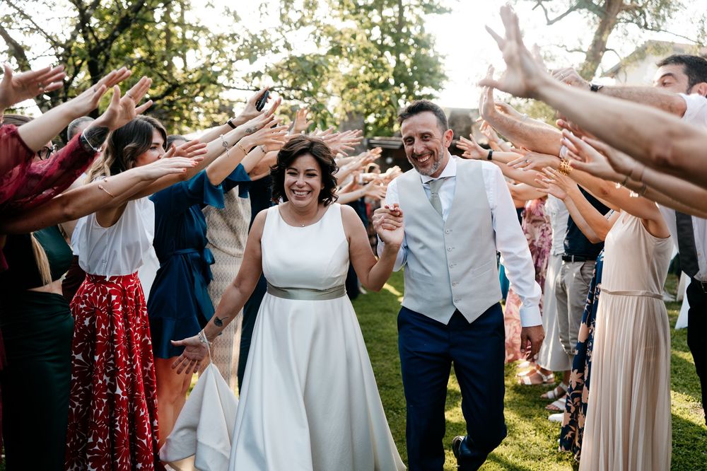 Wedding party celebrates with joyful raised hands forming a tunnel for newlyweds to walk through outdoors.
