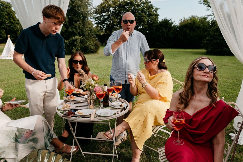 A group enjoys an outdoor summer picnic with drinks and snacks at a garden party on a sunny day.