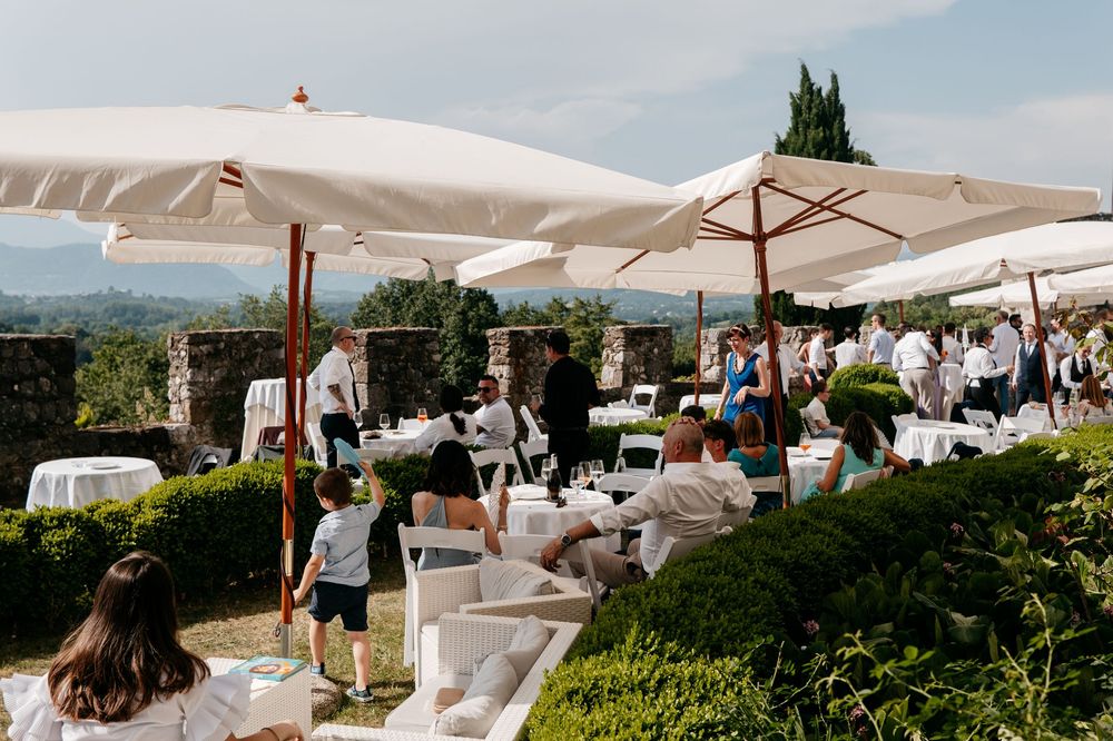 Outdoor restaurant terrace with white umbrellas overlooking a scenic mountain landscape on a sunny day.