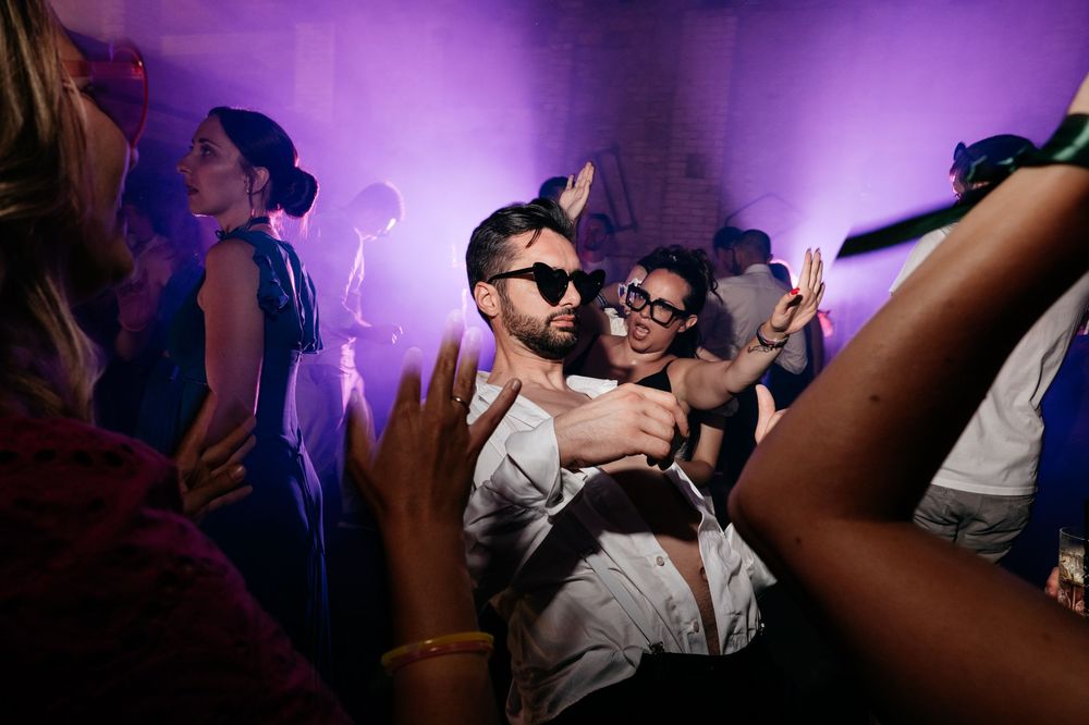 People dancing and enjoying themselves at a nightclub with purple lighting and atmospheric effects.
